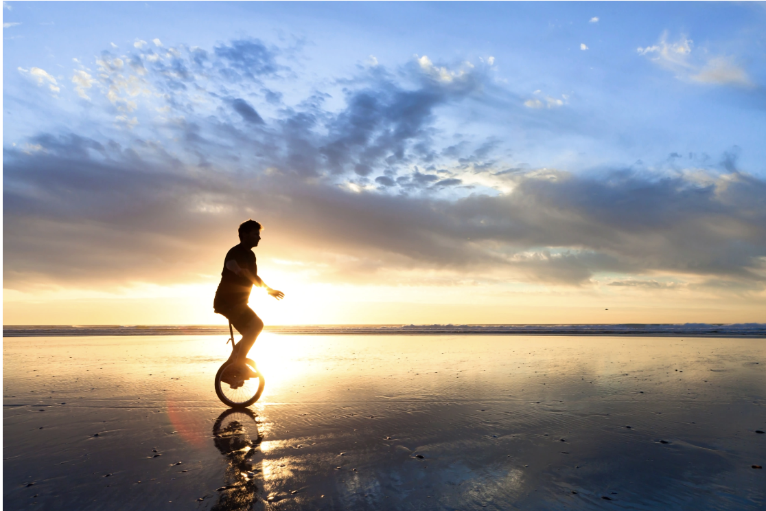 A silhouette of a person riding a unicycle along a reflective wet beach at sunset, evoking the balance, focus, and quiet resilience cultivated through Malachi Gillihan's integrative approach to trauma recovery