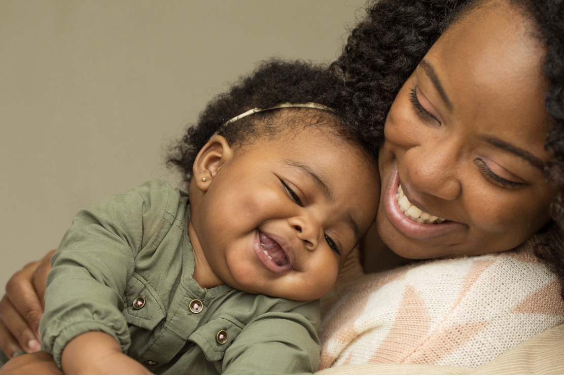 A joyful mother and baby laughing together in a warm embrace, illustrating the secure attachment bond that forms the foundation of healthy development and the attachment healing work offered through Malachi Gillihan's integrative trauma recovery