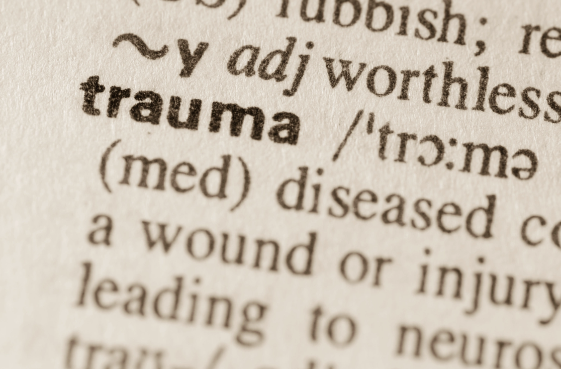 Close-up of a dictionary entry for the word trauma, showing its medical definition as a wound or injury leading to nervous system effects, used in an educational context on the Malachi Gillihan trauma specialist website