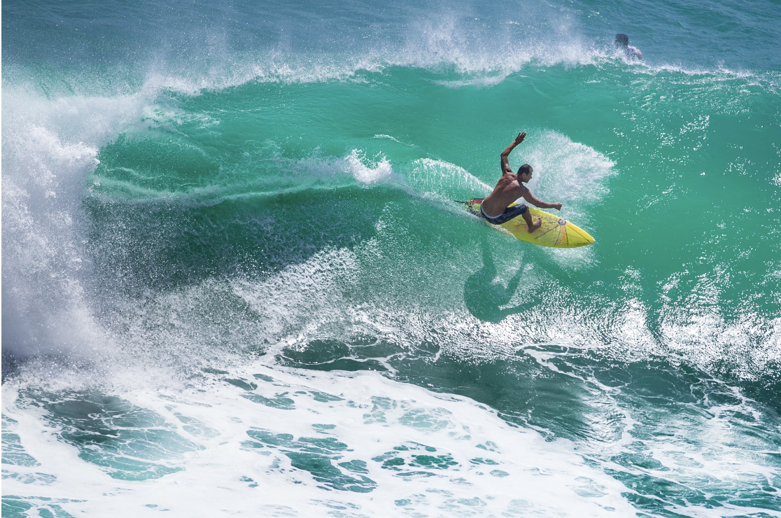 A surfer riding a large turquoise wave on a yellow surfboard, representing the dynamic balance, resilience, and active engagement with difficult emotions that characterizes Malachi Gillihan's approach to trauma recovery