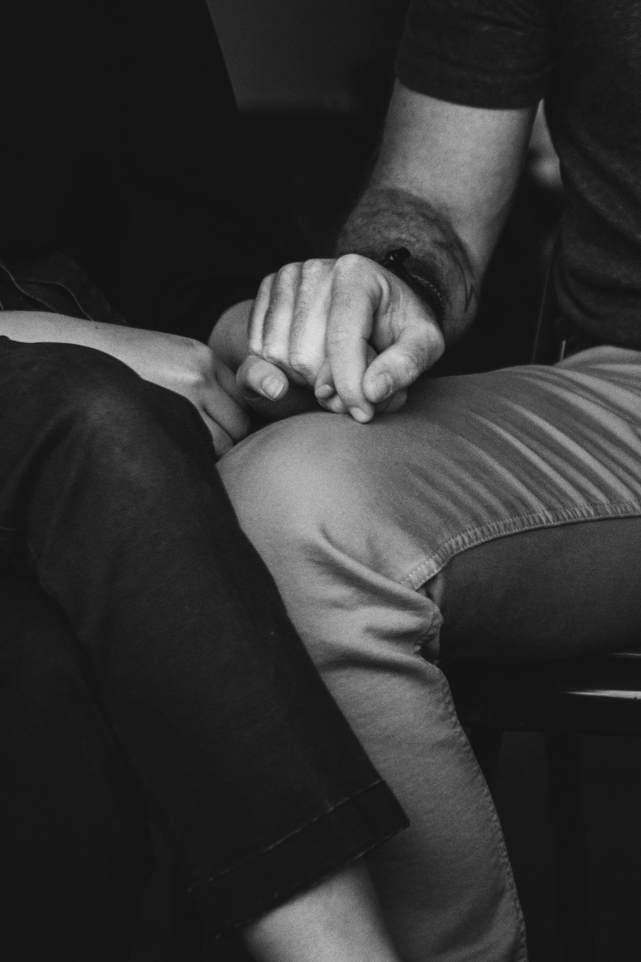 A close-up black and white photograph of one person gently placing their hand on another person's hands in a gesture of comfort and support, evoking the safety, trust, and personal care at the heart of Malachi Gillihan's trauma recovery practice