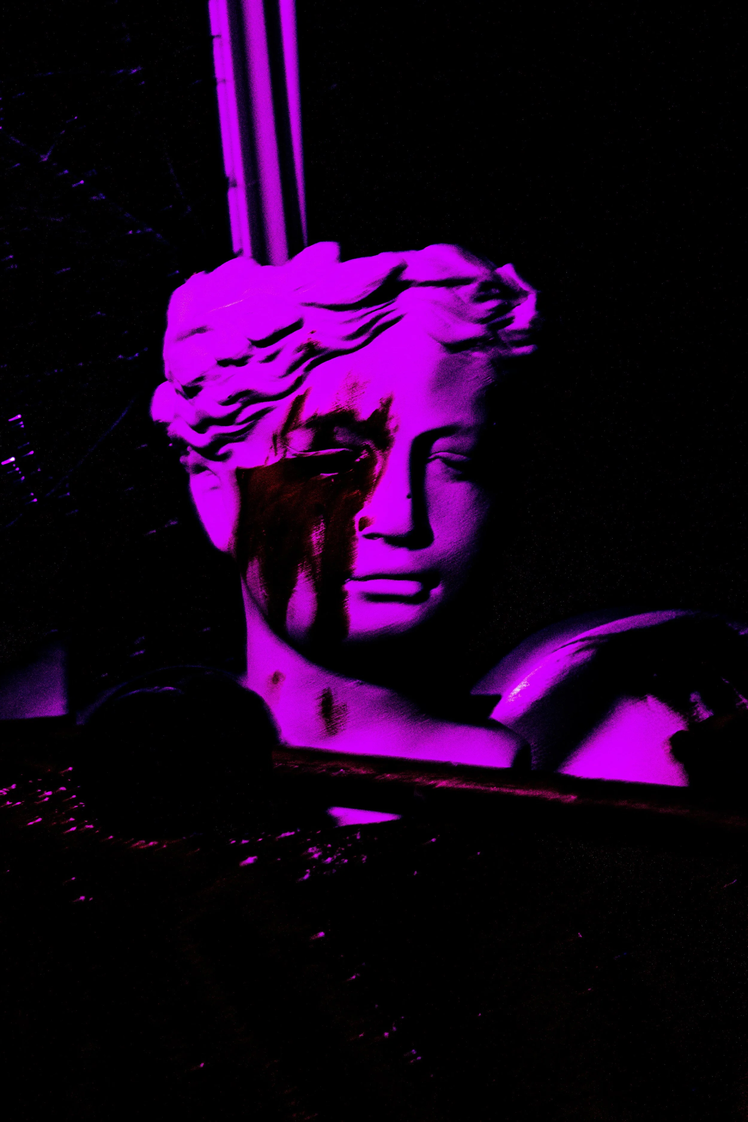 A classical-style sculpture bust illuminated in purple light, with what appears to be dripping red paint on the face, set against a dark background.