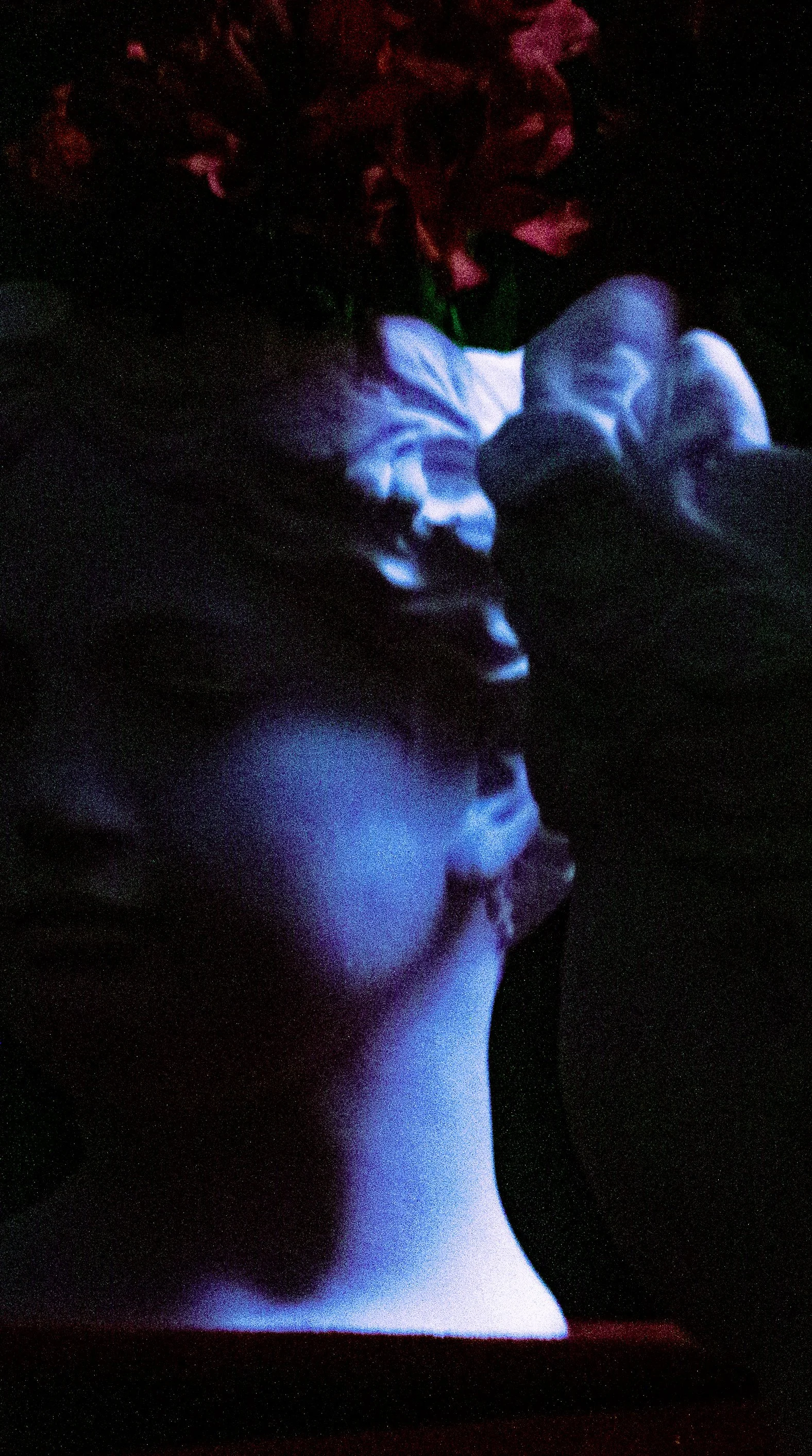 Close-up of a dimly lit marble bust with a floral headdress, casting soft shadows and highlighted in blue and red light.
