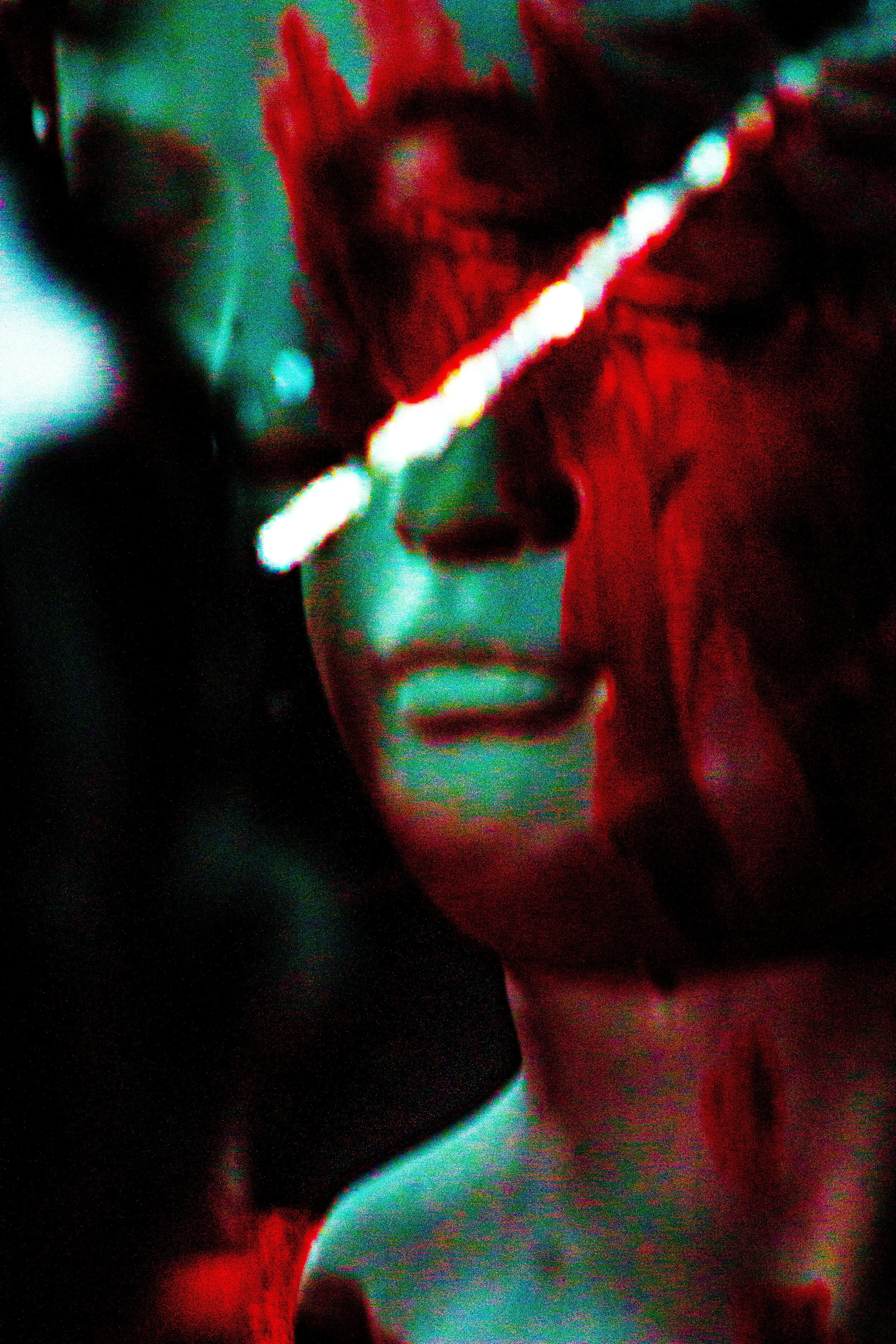 Abstract image with red and turquoise hues, focusing on a distorted human-like face partially obscured by a bright diagonal line.