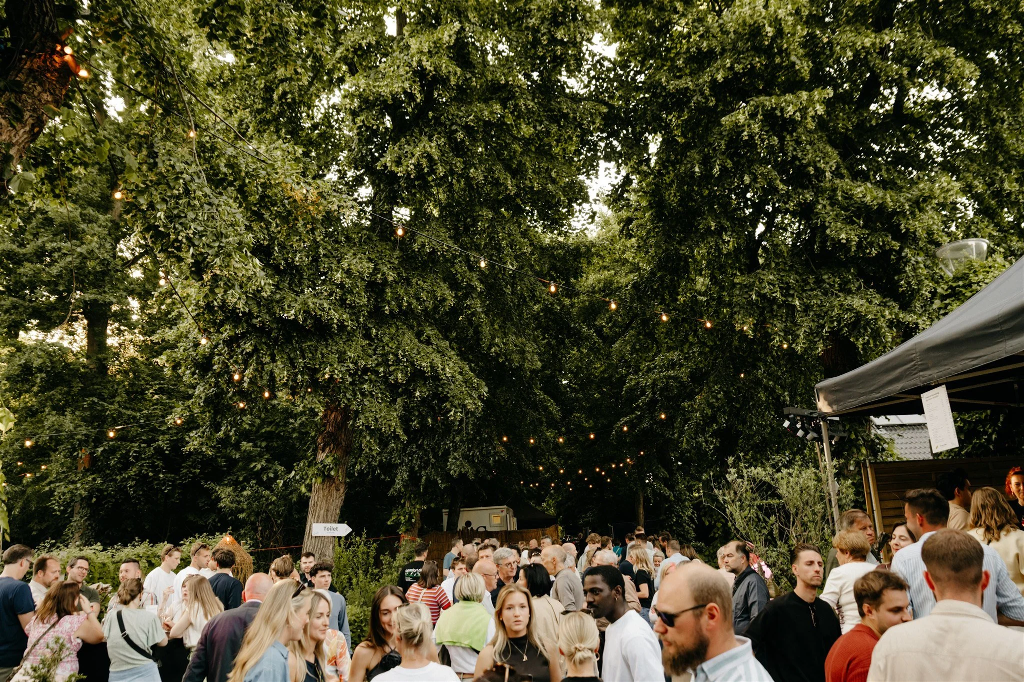 Groep mensen poseert buiten voor een houten terras met een tent en planten.