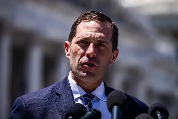 A man in a suit speaking into microphones during an outdoor press conference