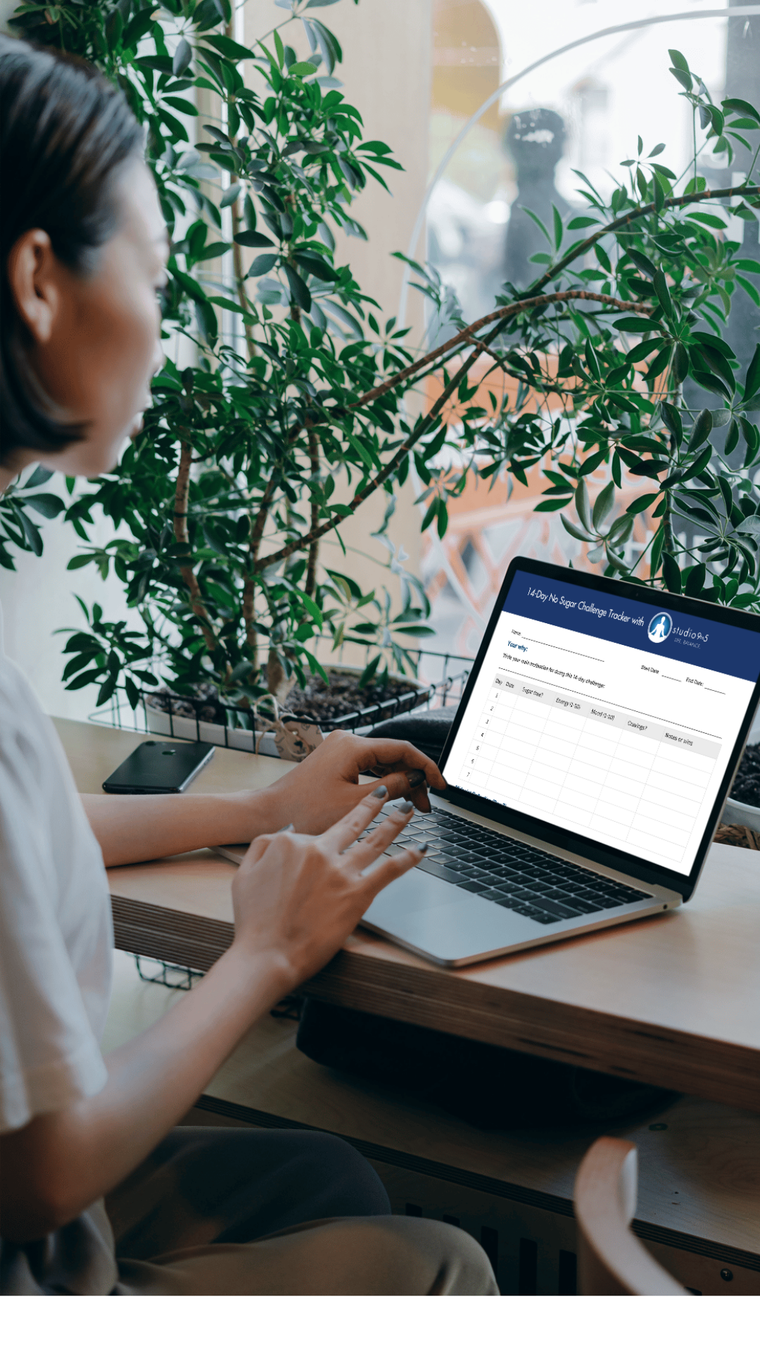 Person working on a laptop in a modern office setting with greenery, representing digital wellness tools and workplace wellbeing programs.