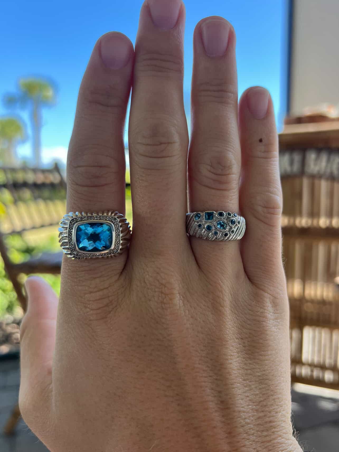 A hand showing two silver rings with blue topaz stones.