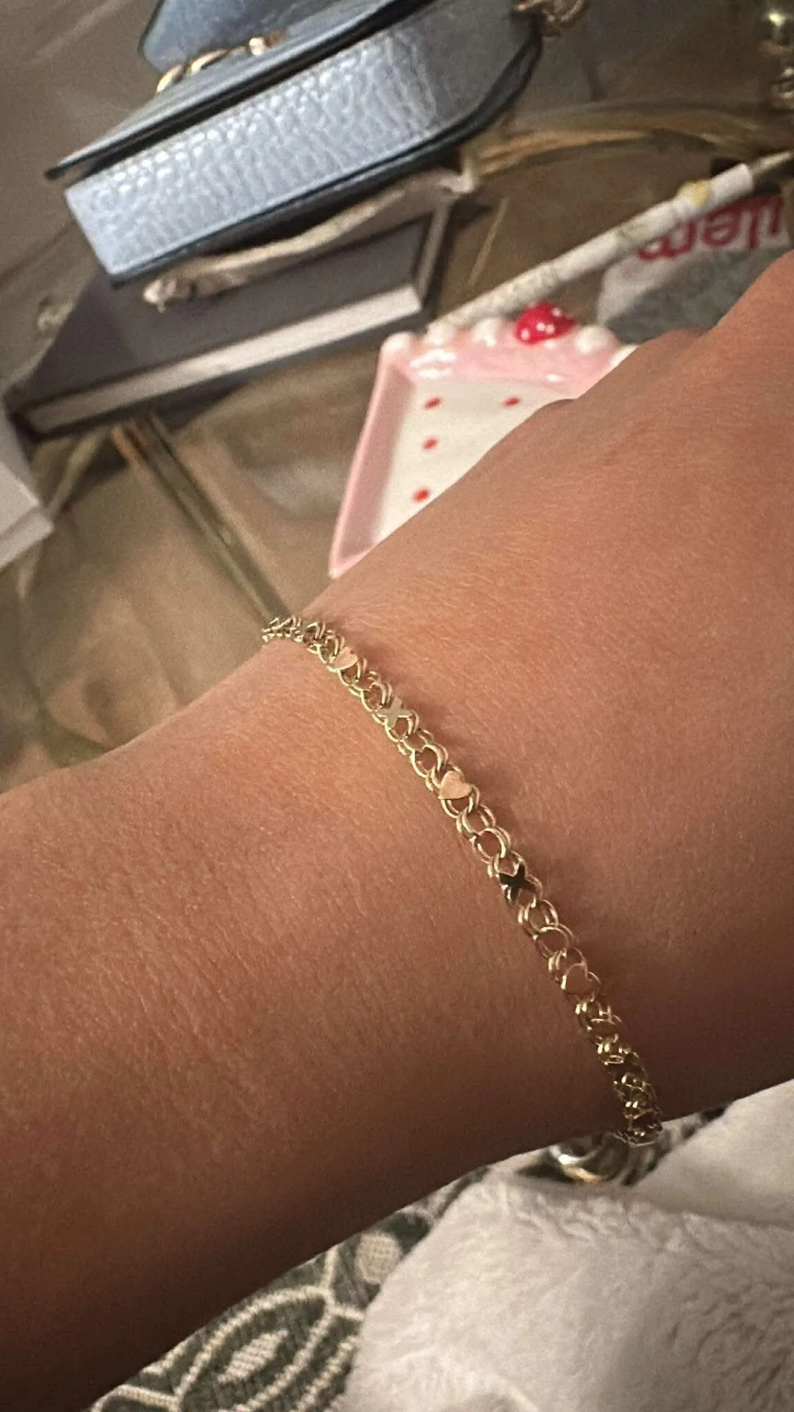 Someone's wrist displaying a yellow gold bracelet with rose gold hearts and yellow gold Xs.