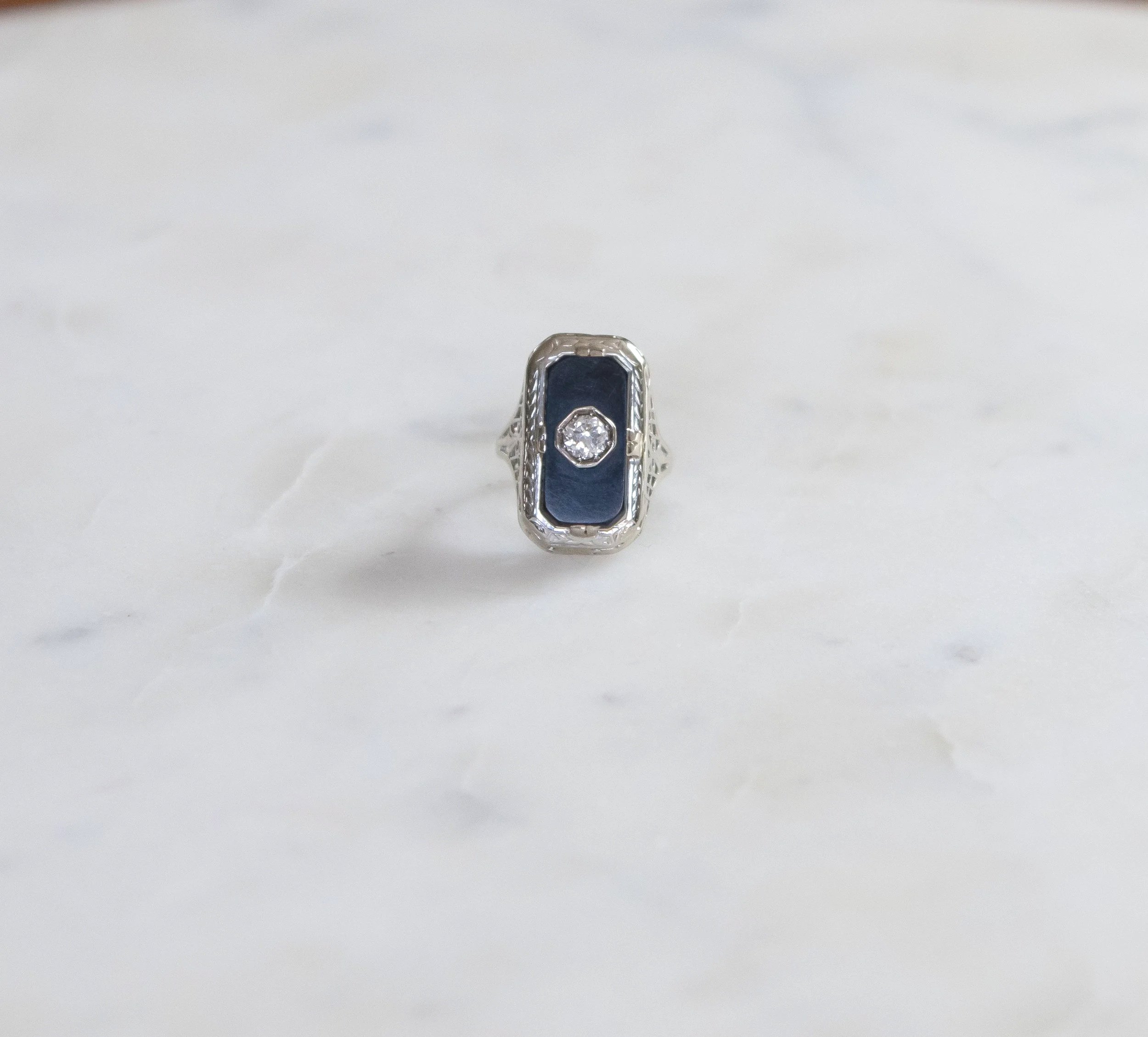 A 14k white gold Art Deco ring with a large rectangular onyx embedded with a diamond in the center.