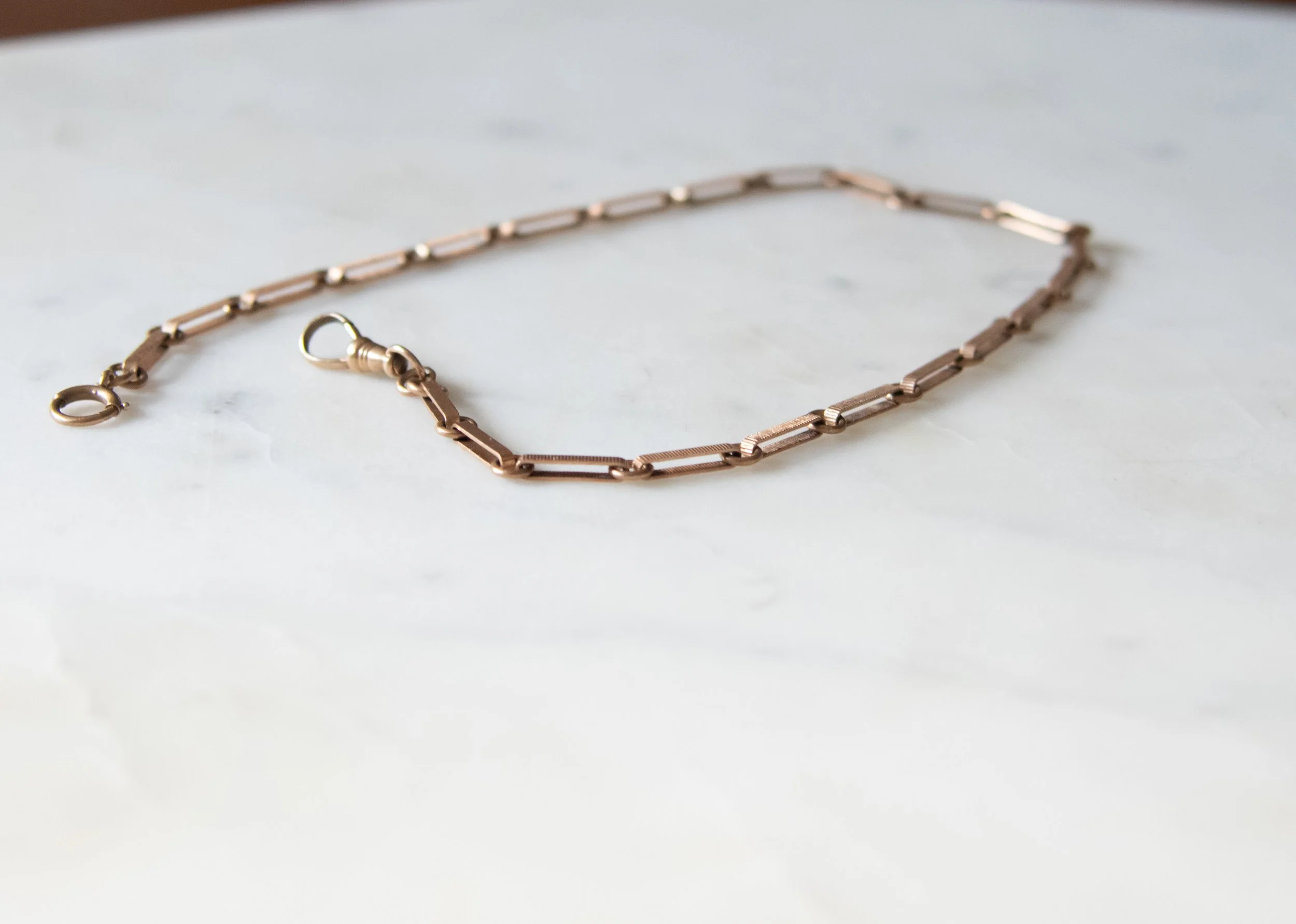 The side view of a rose gold watch chain with elongated open links.