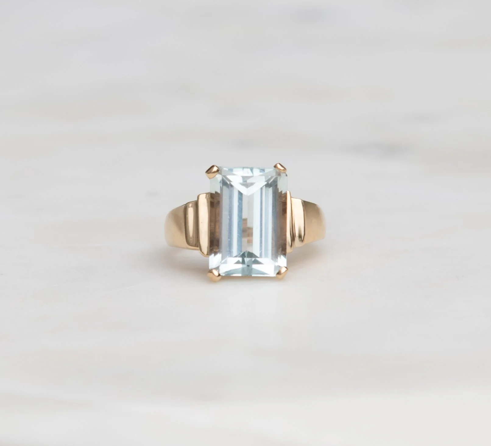 A gold ring with a large light blue emerald-cut aquamarine.