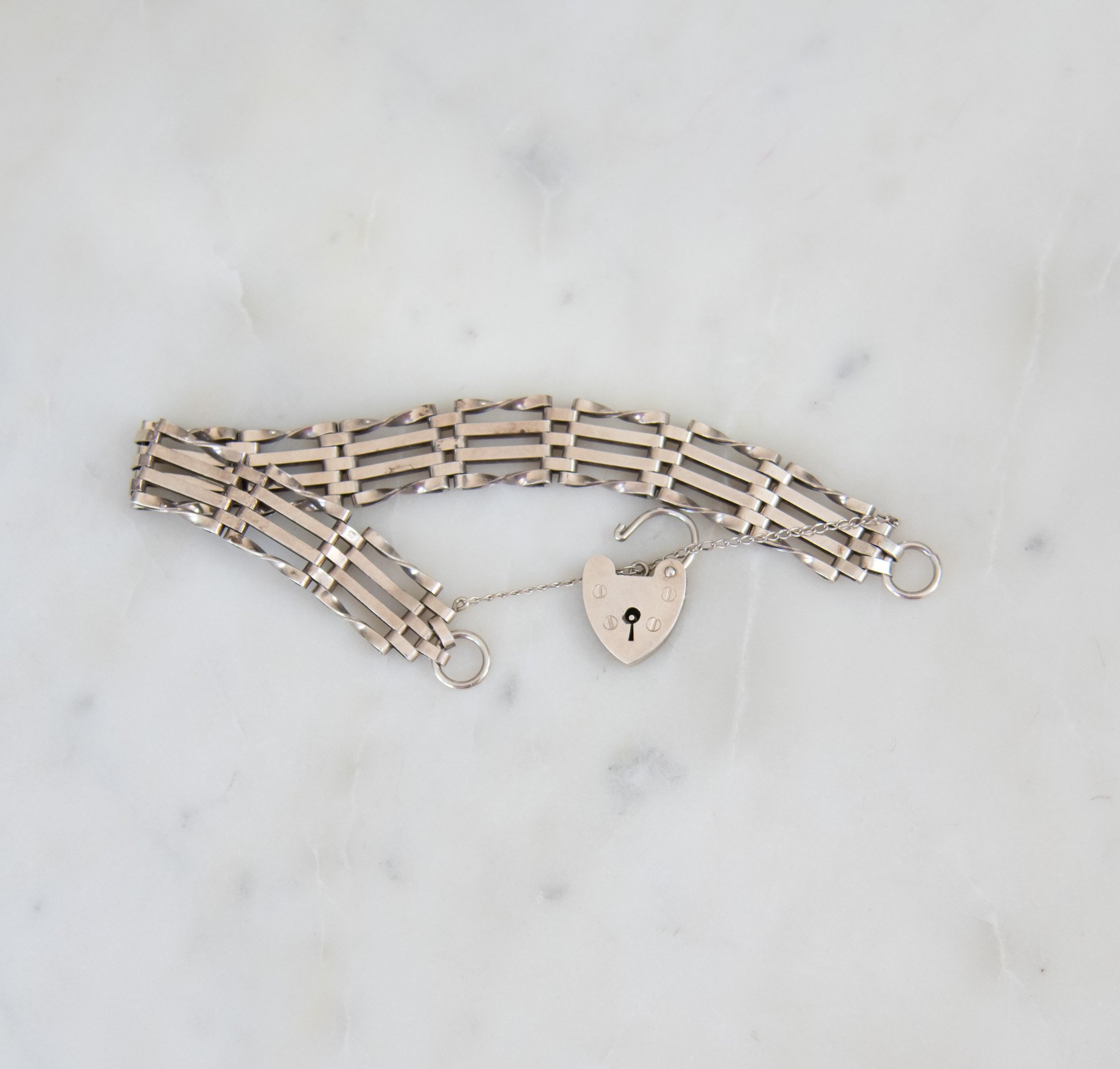 Silver bracelet with rectangular open link design and a heart-shaped padlock connector.