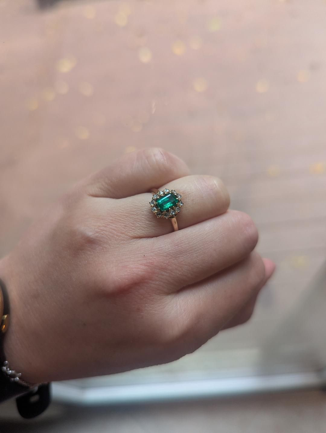 A hand wearing a gold emerald and diamond ring.
