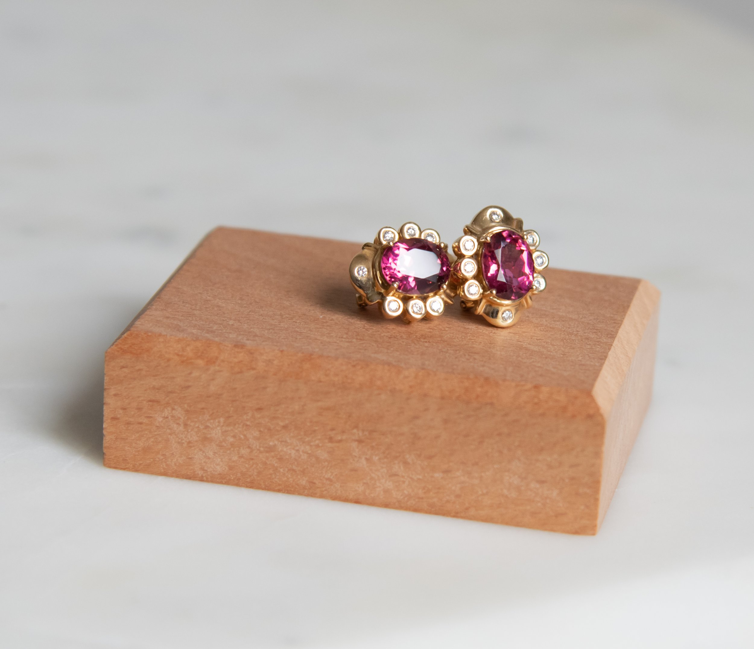 14K gold earrings with large pink tourmaline stones surrounded by diamonds in a satellite halo.