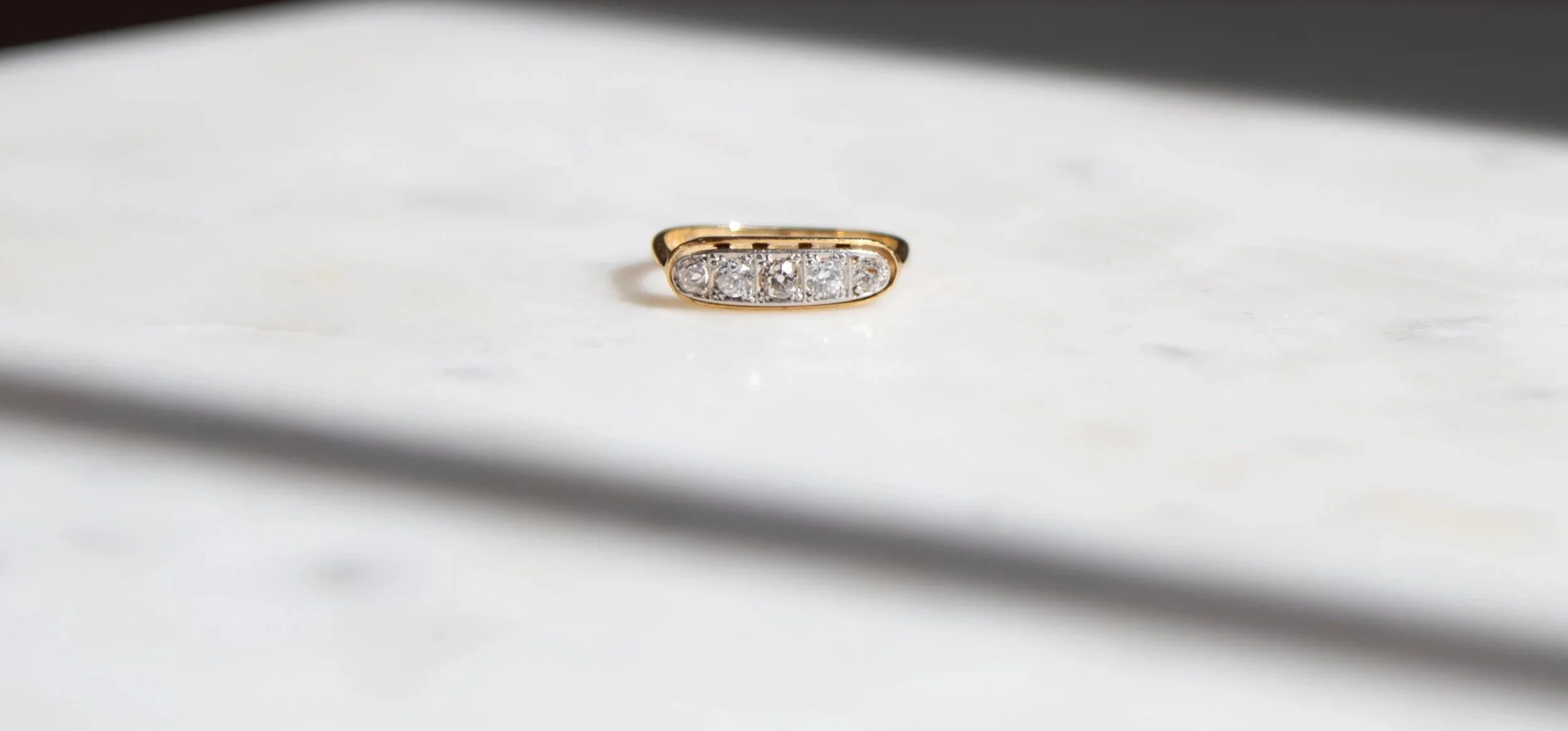 A gold ring with 5 diamonds against a white stone surface.