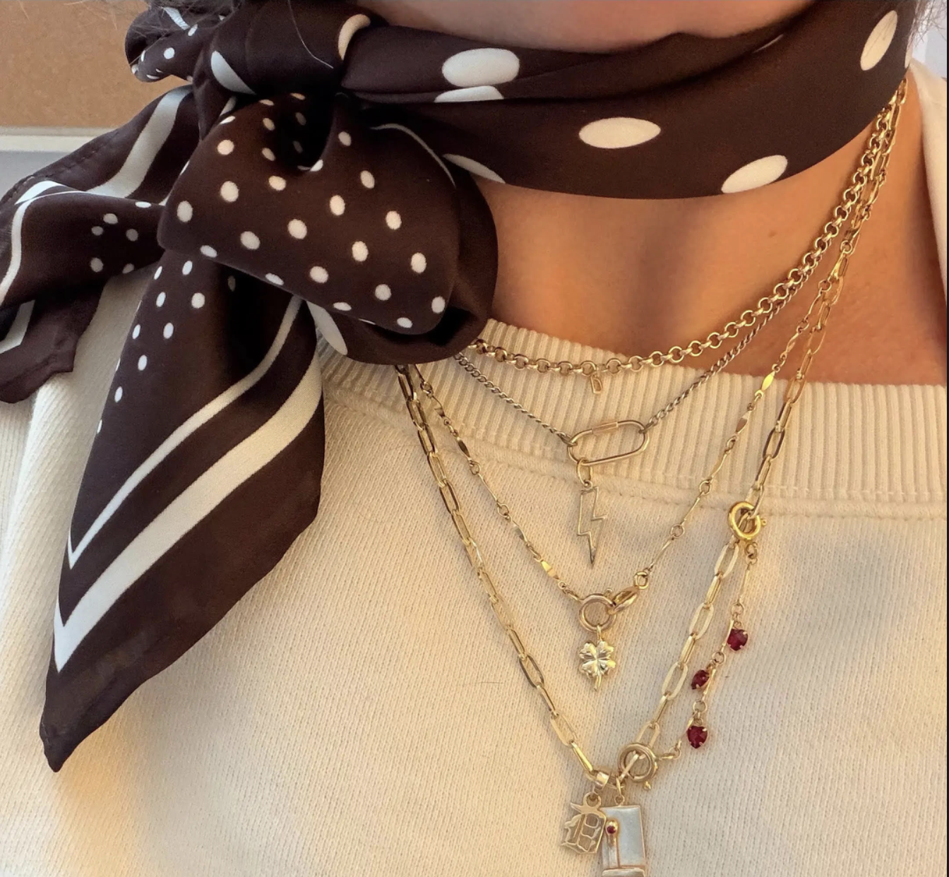 A close-up image of a neck wearing a brown and white scarf and gold chains of various lengths.