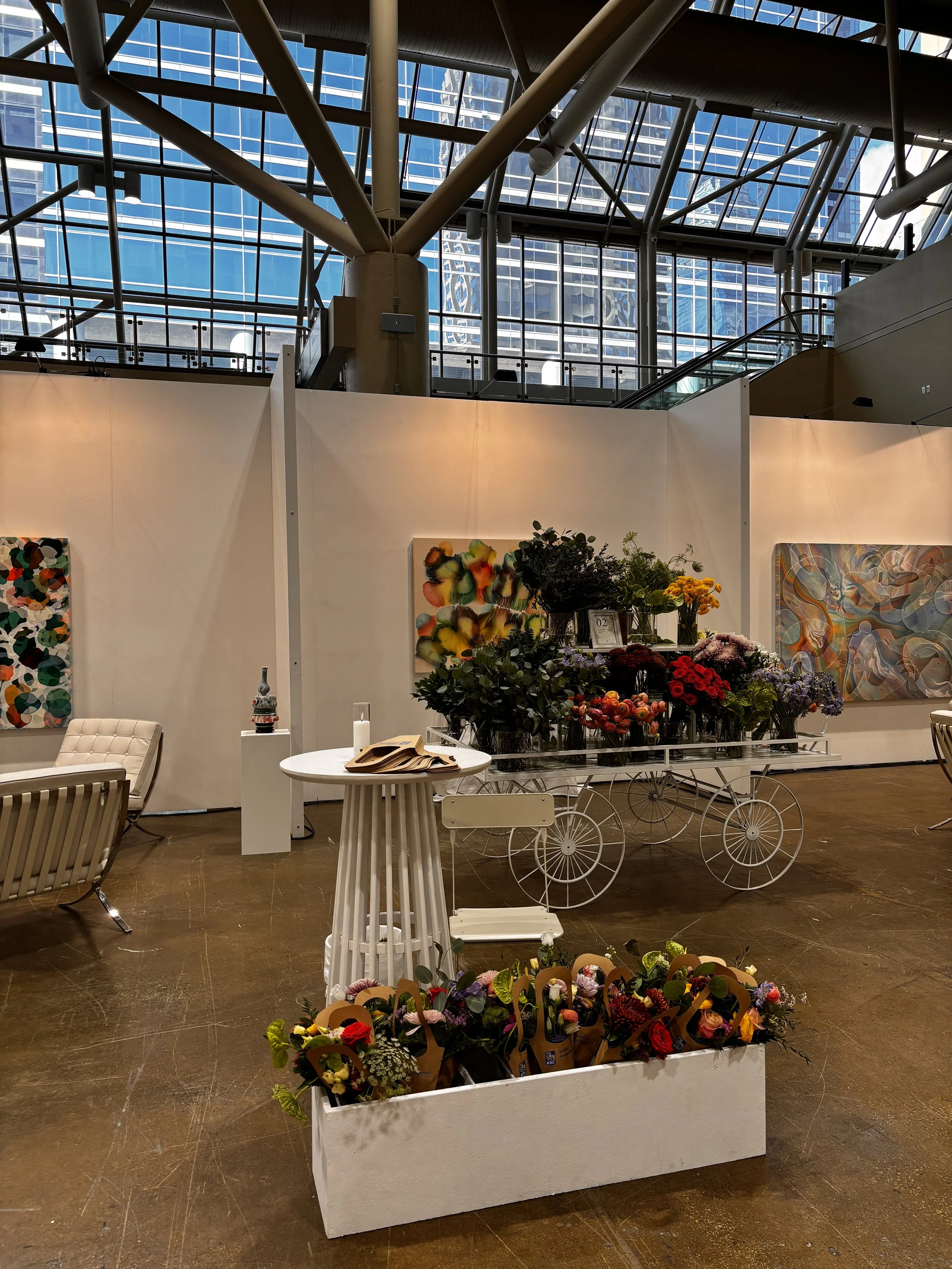 Art gallery interior with floral arrangements, paintings, and seating areas.