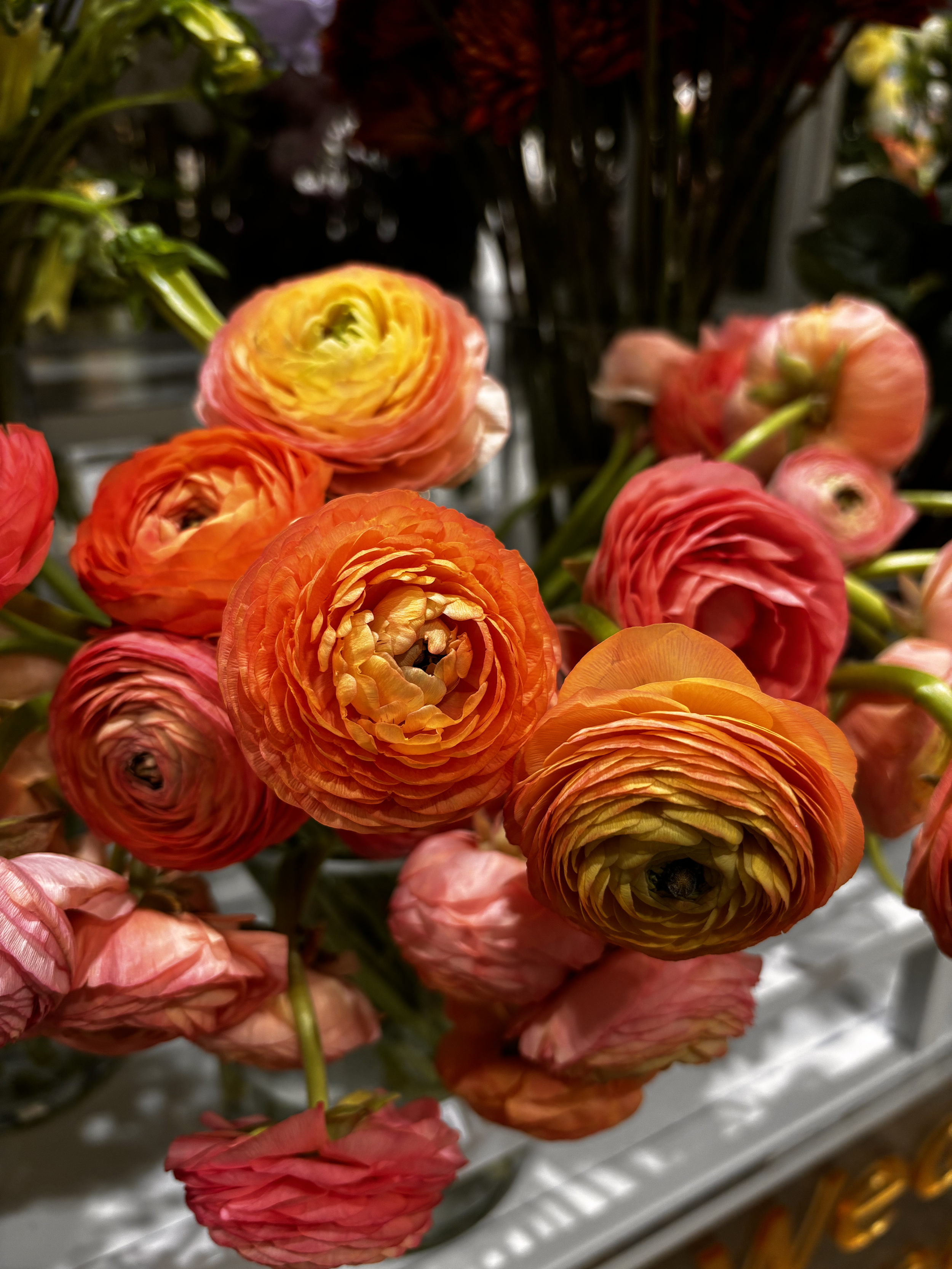 Close-up of a bouquet of colorful ranunculus flowers in shades of yellow, orange, pink, and red.