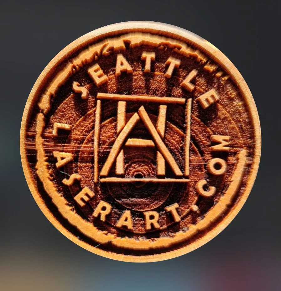 Round wooden token with engraved design and text reading "Statelace 4th of July Party." The design resembles a festival or carnival emblem, with geometric shapes and lines.