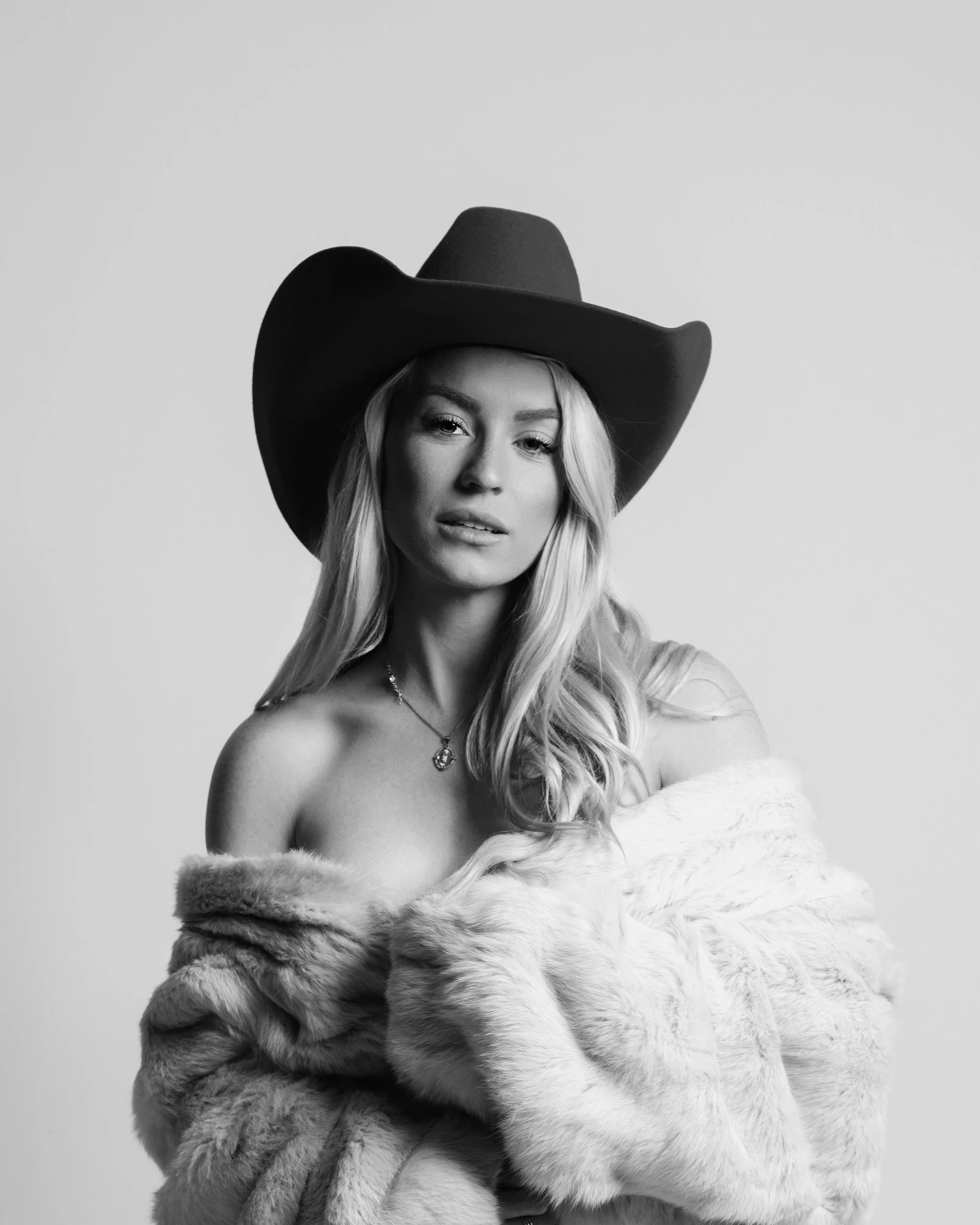 Black and white portrait of a woman wearing a large cowboy hat and a fur coat.