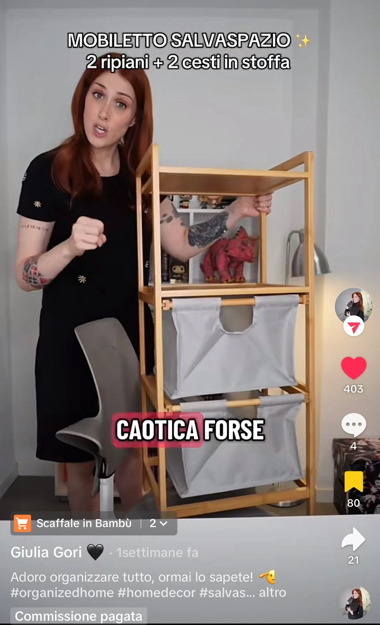 Una donna con capelli rossi mostra un mobiletto in legno con scomparti in tessuto. Sullo schermo ci sono scritte delle descrizioni in italiano, tra cui 'Mobiletto salvaspazio', '2 ripiani + 2 cesti in stoffa', e 'Caotica forse'.