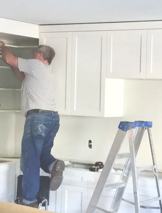 Bob and Marks craftsman installing custom white shaker upper cabinets during kitchen renovation Pembroke Ontario