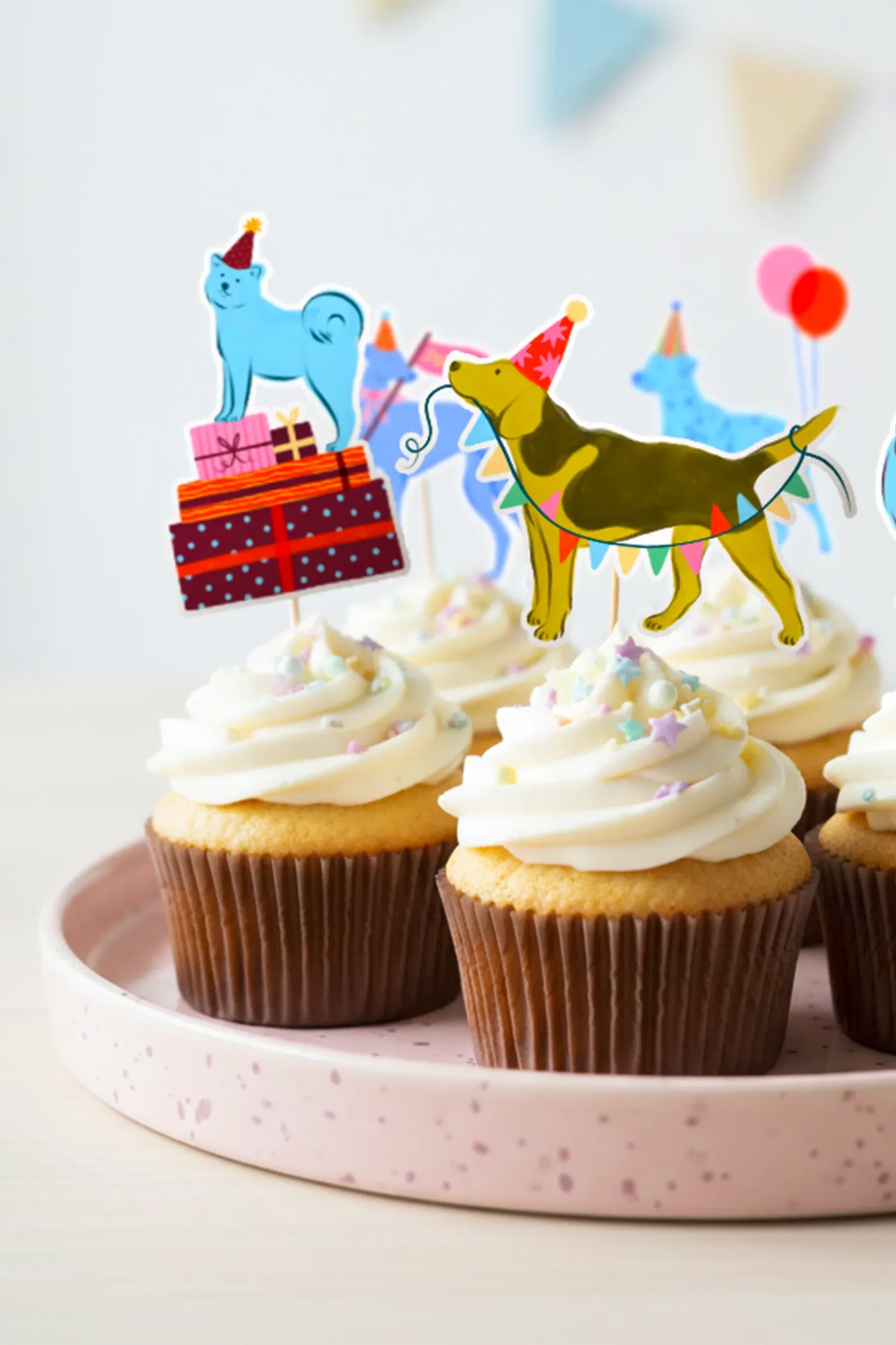 Cupcakes décorés avec des figurines de chiens portant des chapeaux de fête et des guirlandes, avec des étoiles et des perles en sucre colorées.