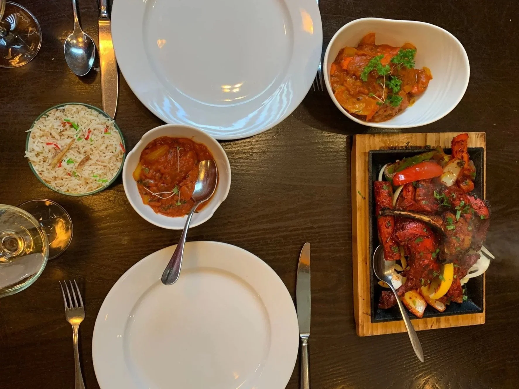 A top view of a dinner table with white plates, silverware, and various Indian dishes including rice, curry, and tandoori chicken.
