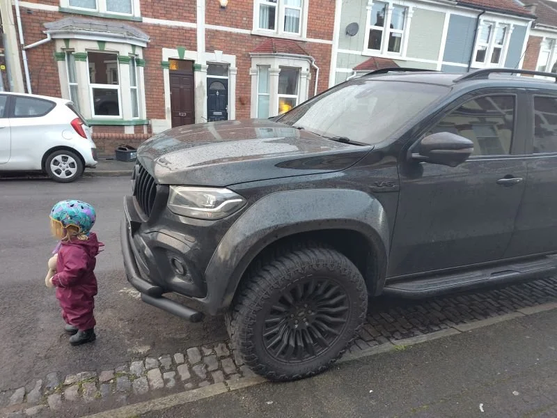 Image shows a small child standing in front of a large, high-bonneted pickup truck.