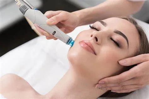 A woman receiving a cosmetic treatment with a pen-shaped device on her cheek in a spa or clinic setting.