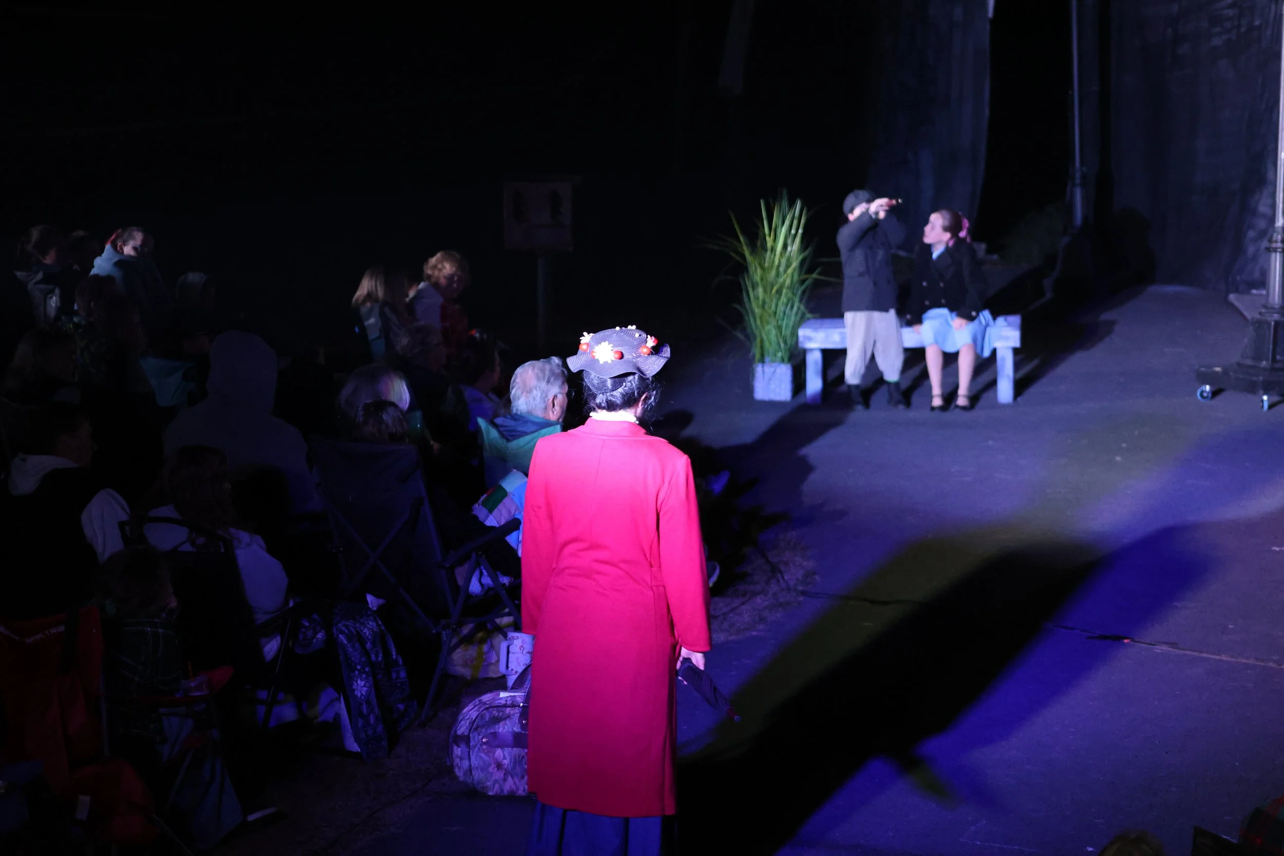 People watching a theatrical performance on an outdoor stage at night.
