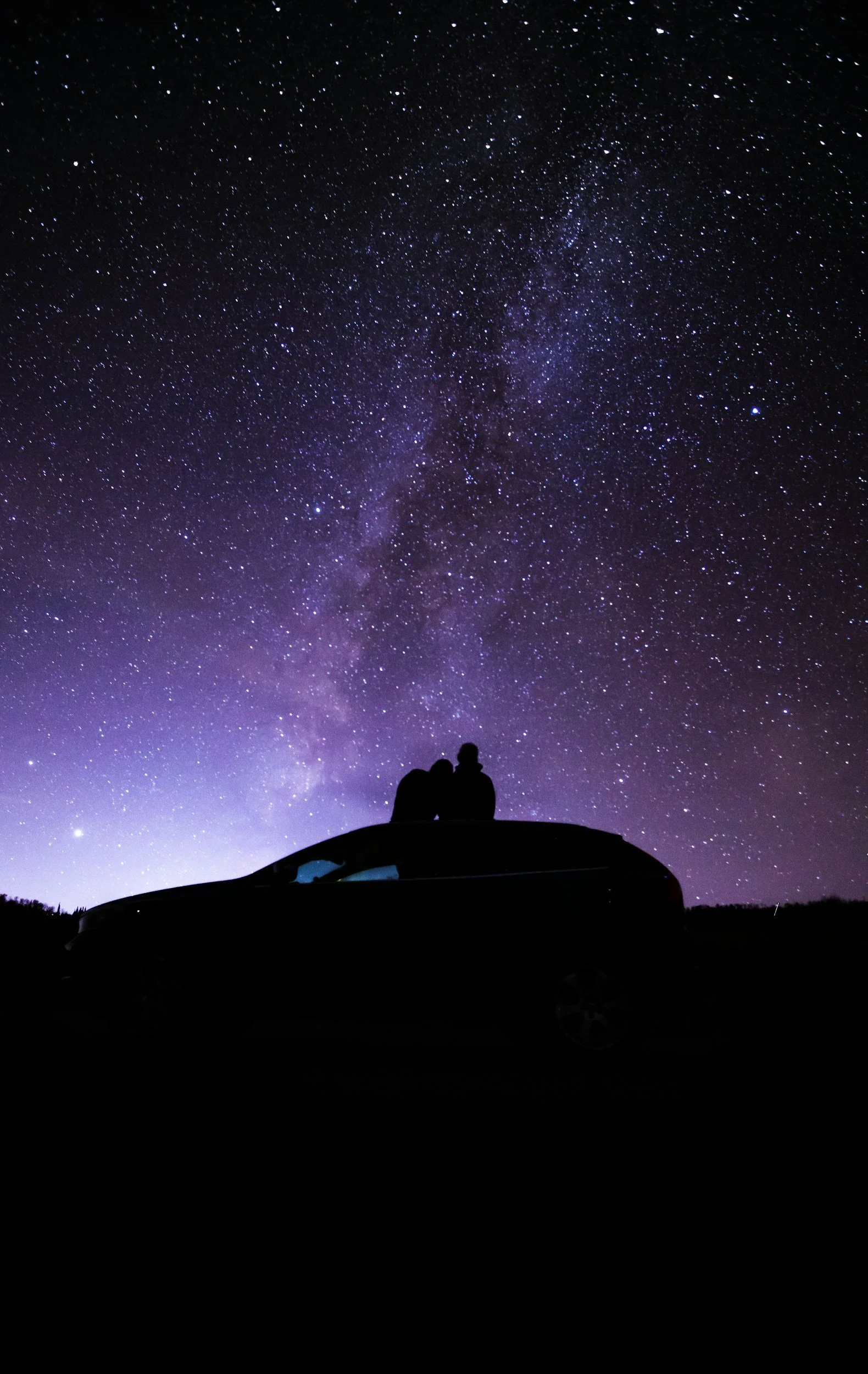a couple after a relationship reading sitting looking at the night sky ontop their car