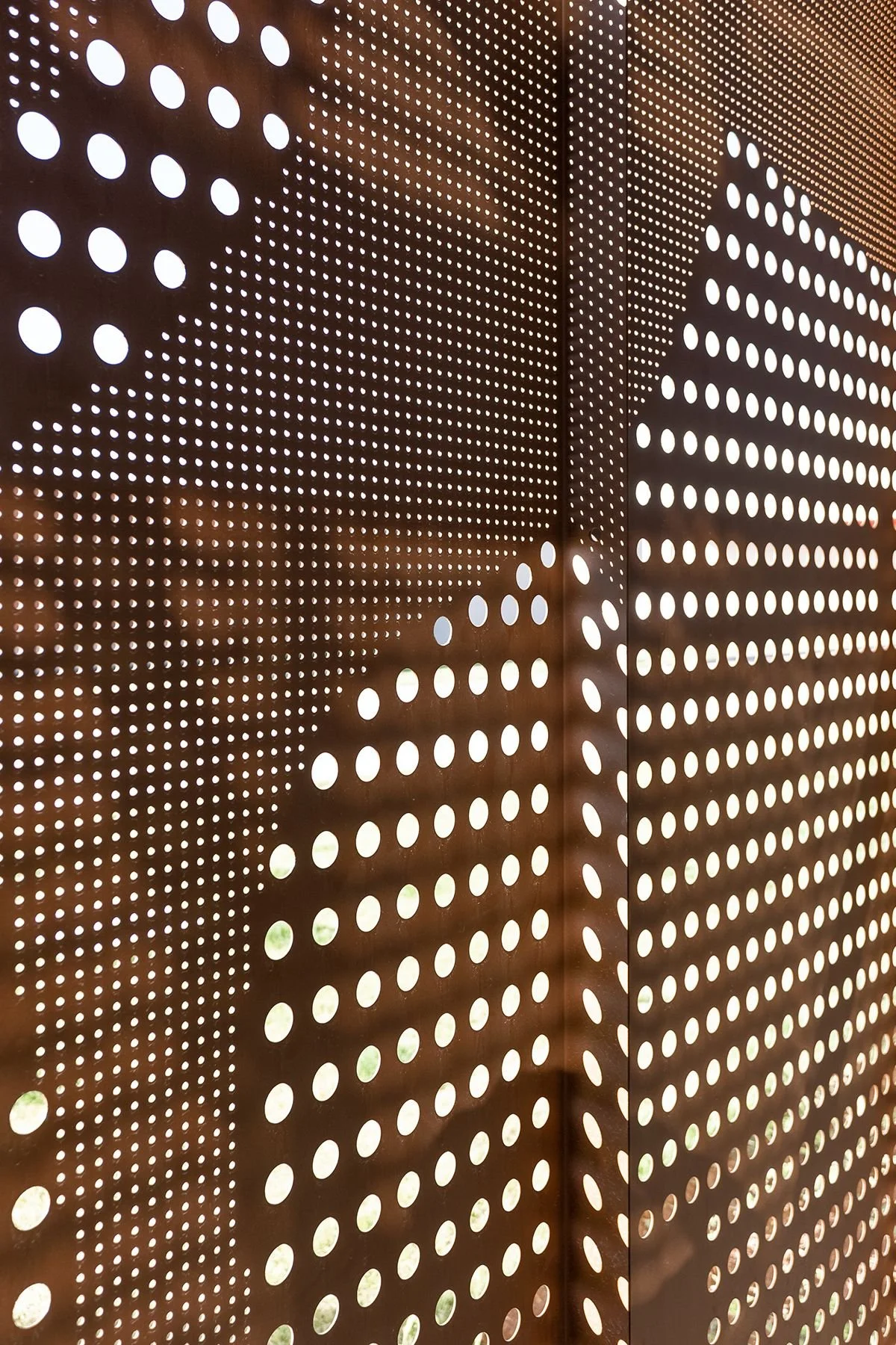 Close-up view of a perforated metal wall with circular holes, creating abstract patterns and letting light through.