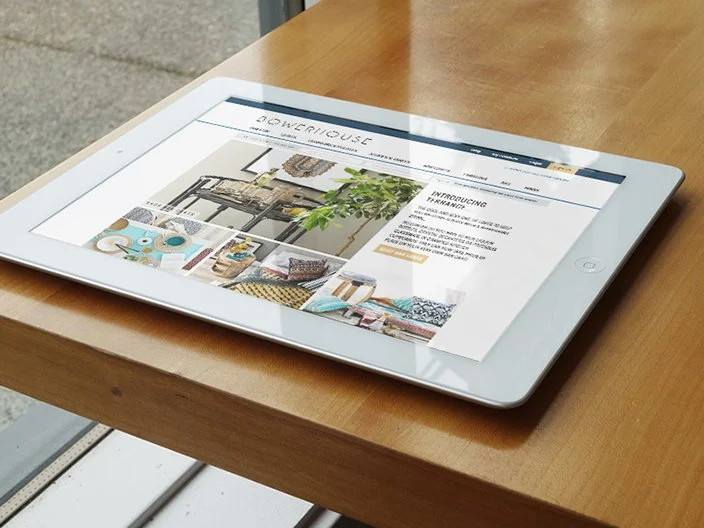 A white tablet on a wooden table displaying a website named 'Powerhouse' with images of interior decor and furniture.