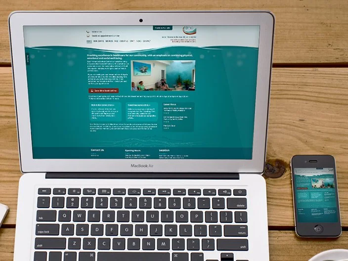 A MacBook Air and an iPhone displaying the same website on a wooden table.