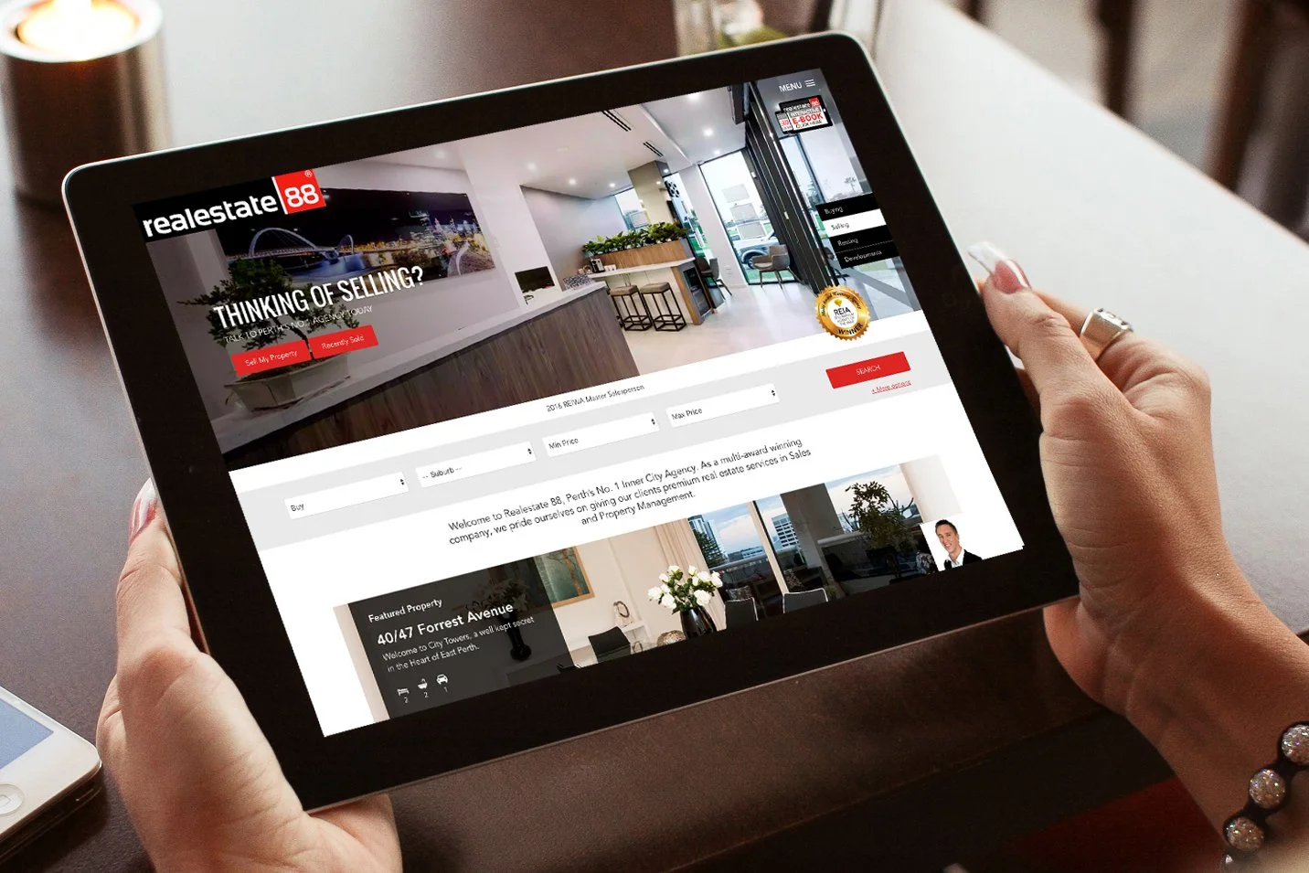 Person holding a tablet displaying a real estate website with images of an interior space, featuring a contemporary kitchen and living area.