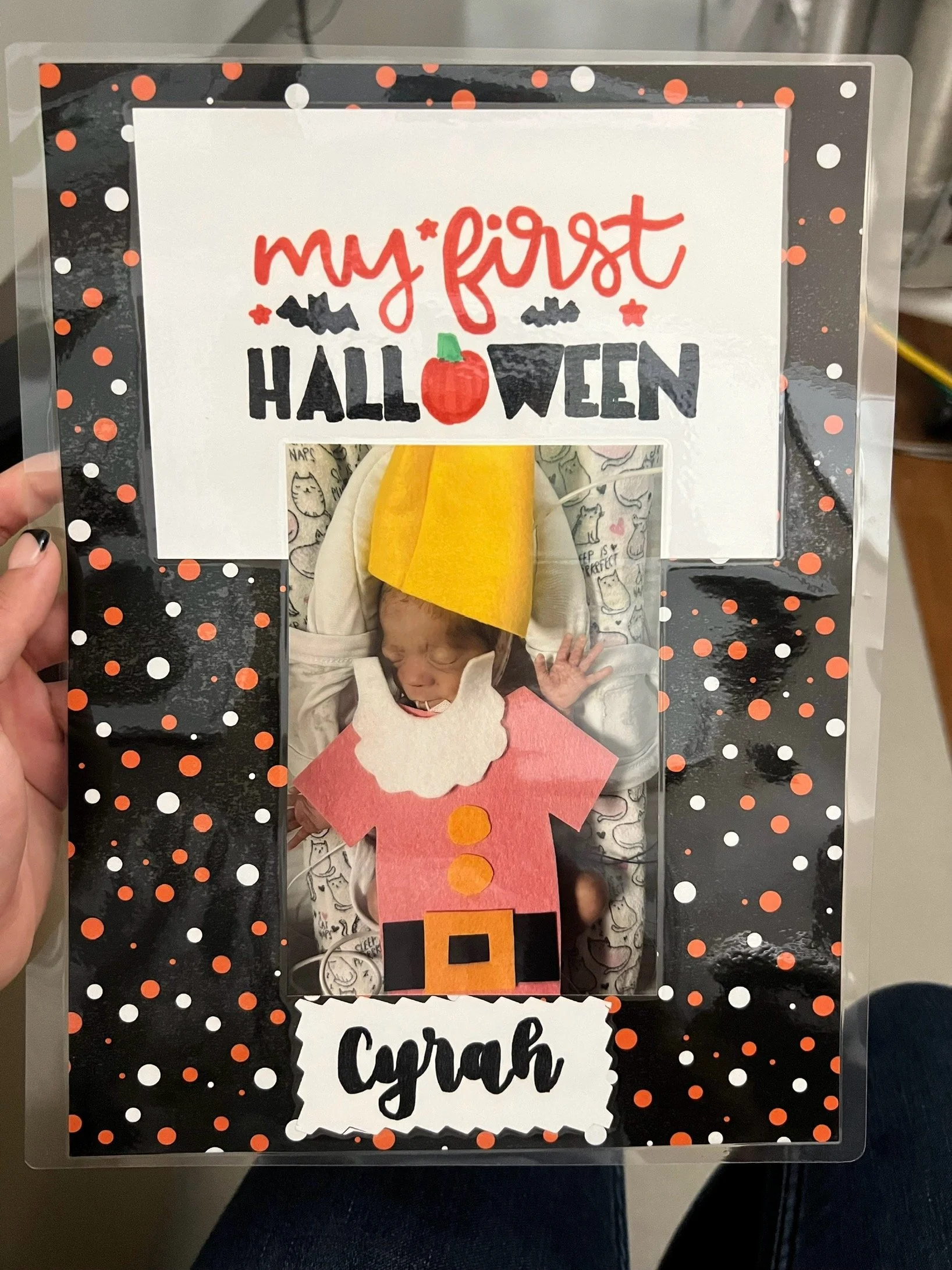 A newborn dressed as a gnome for Halloween with a sign that says my first HALLOWEEN and the name Cyrah..