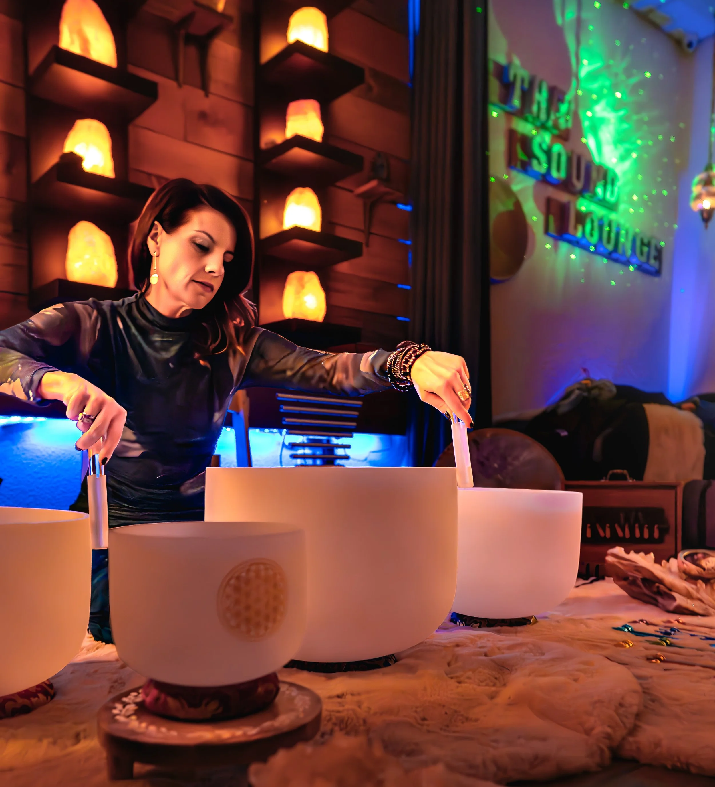 A woman with dark hair is sitting at a table with salt and pepper shakers, colorful confetti and small candles, in a dimly lit restaurant decorated with salt lamps and a neon sign reading 'The Young'.