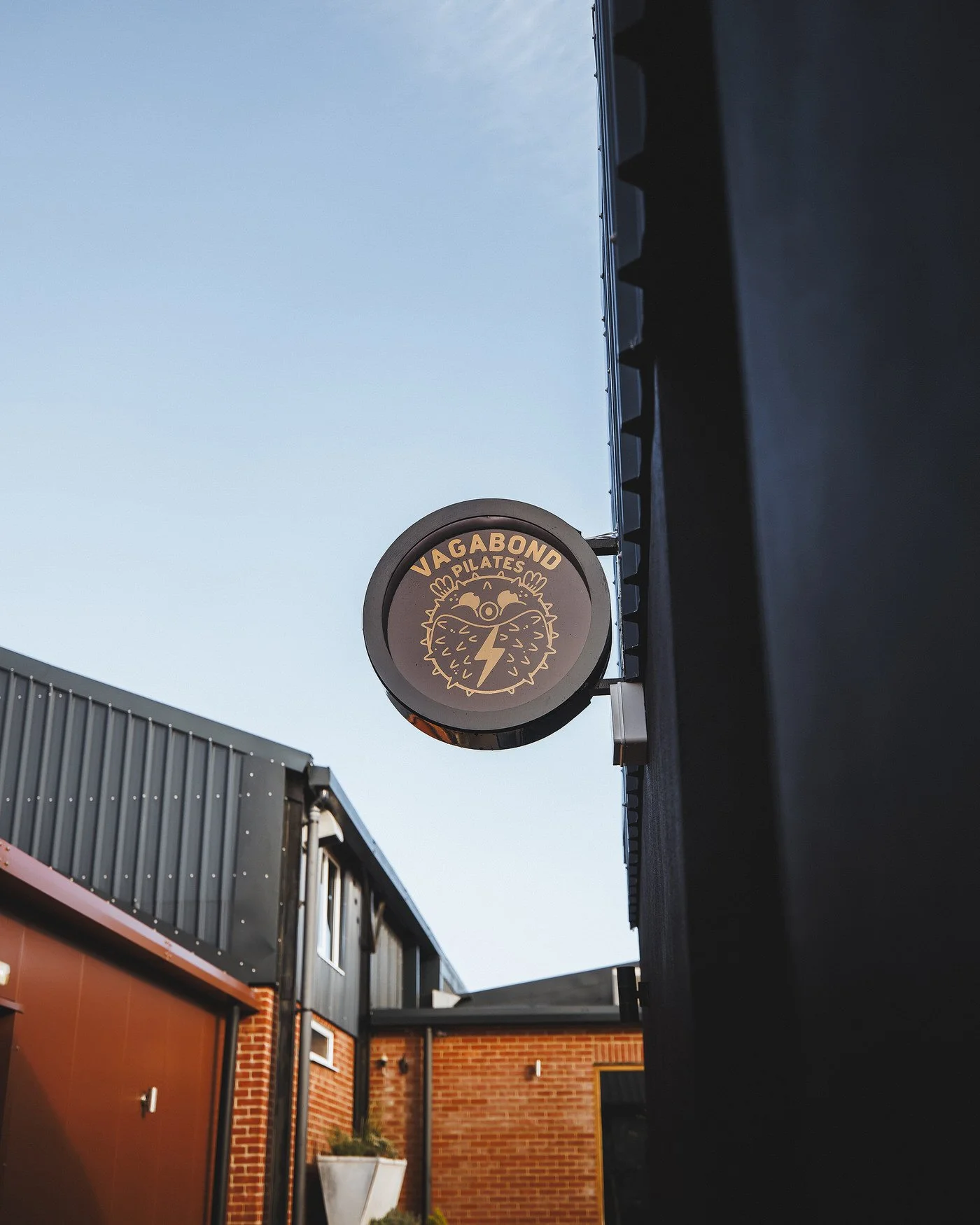 Sign for Vagabond Pilates with a stylized lion face logo, mounted on an exterior building wall.