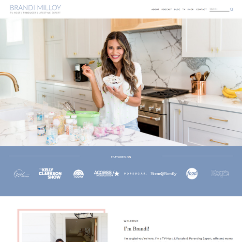 A woman in a white kitchen holds a bowl of decorated cookies, smiling.