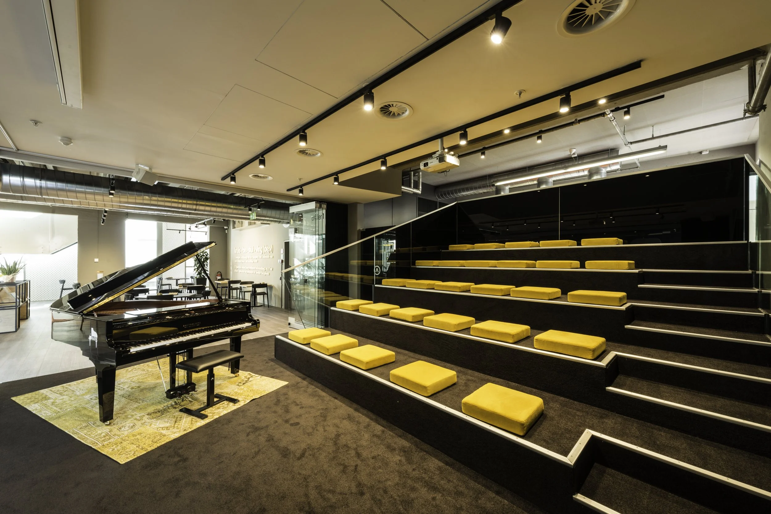 Auditorium met vleugel piano en gele zacht kussentjes om plaats te nemen 