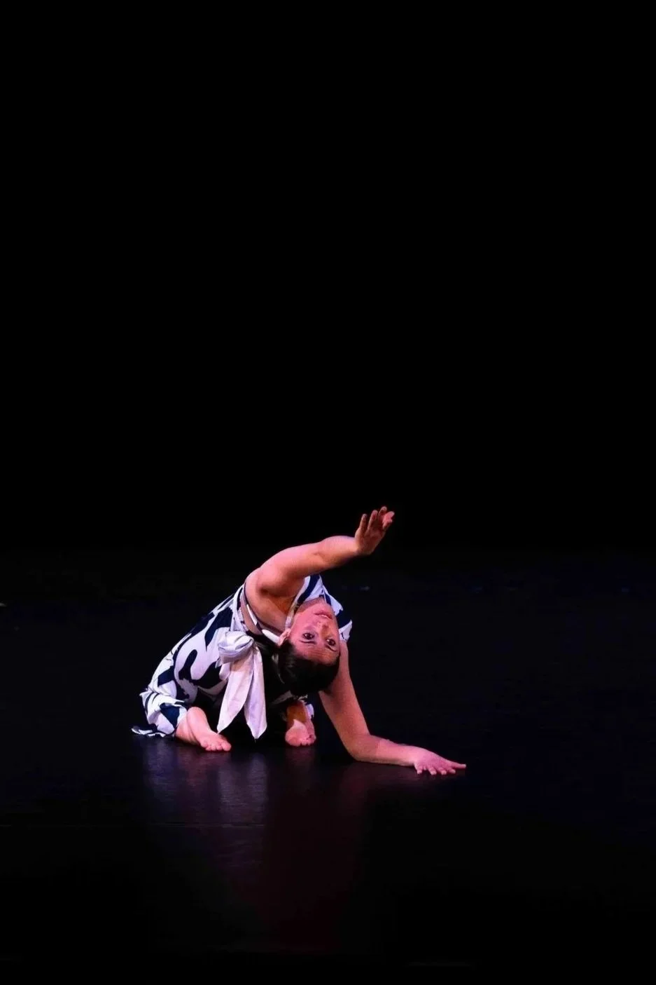 Dancer on knees facing away from the camera, but leaning back and reaching toward, with her gaze at the camera.