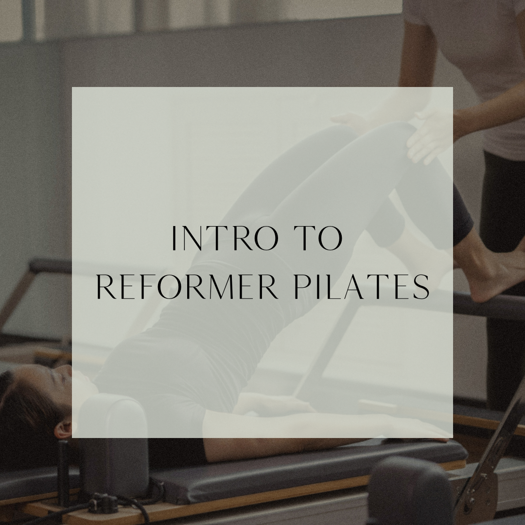 Person lying on reformer Pilates machine during class, instructor assisting in background.