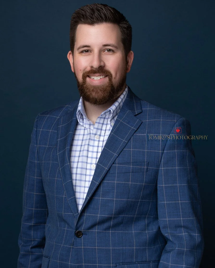 Professional studio headshot of a confident male executive in formal business attire, showcasing a polished and authoritative demeanor.
