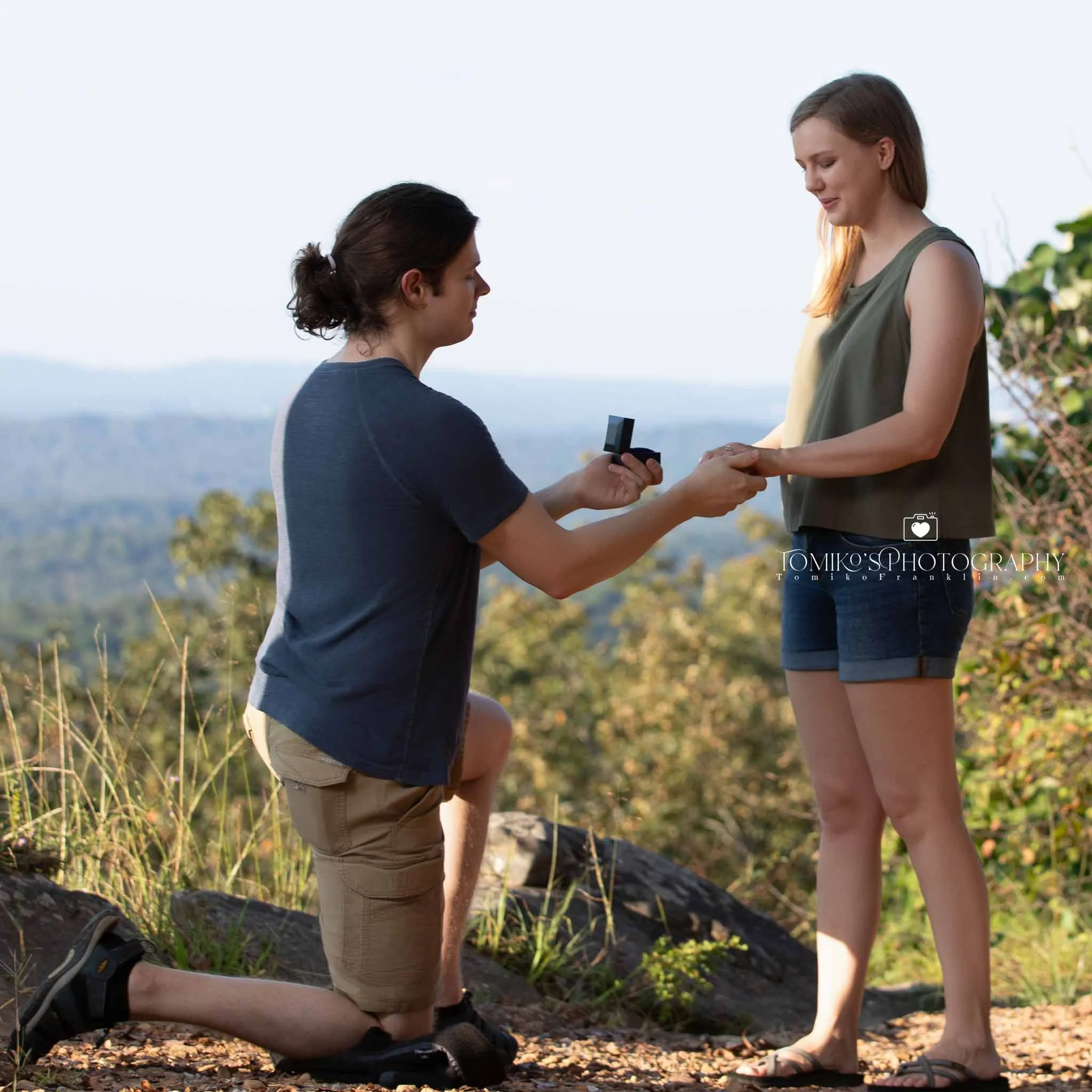 He kneels to propose overlooking the scenic lake at Oak Mountain State Park near Birmingham AL, photographed discreetly and elegantly.