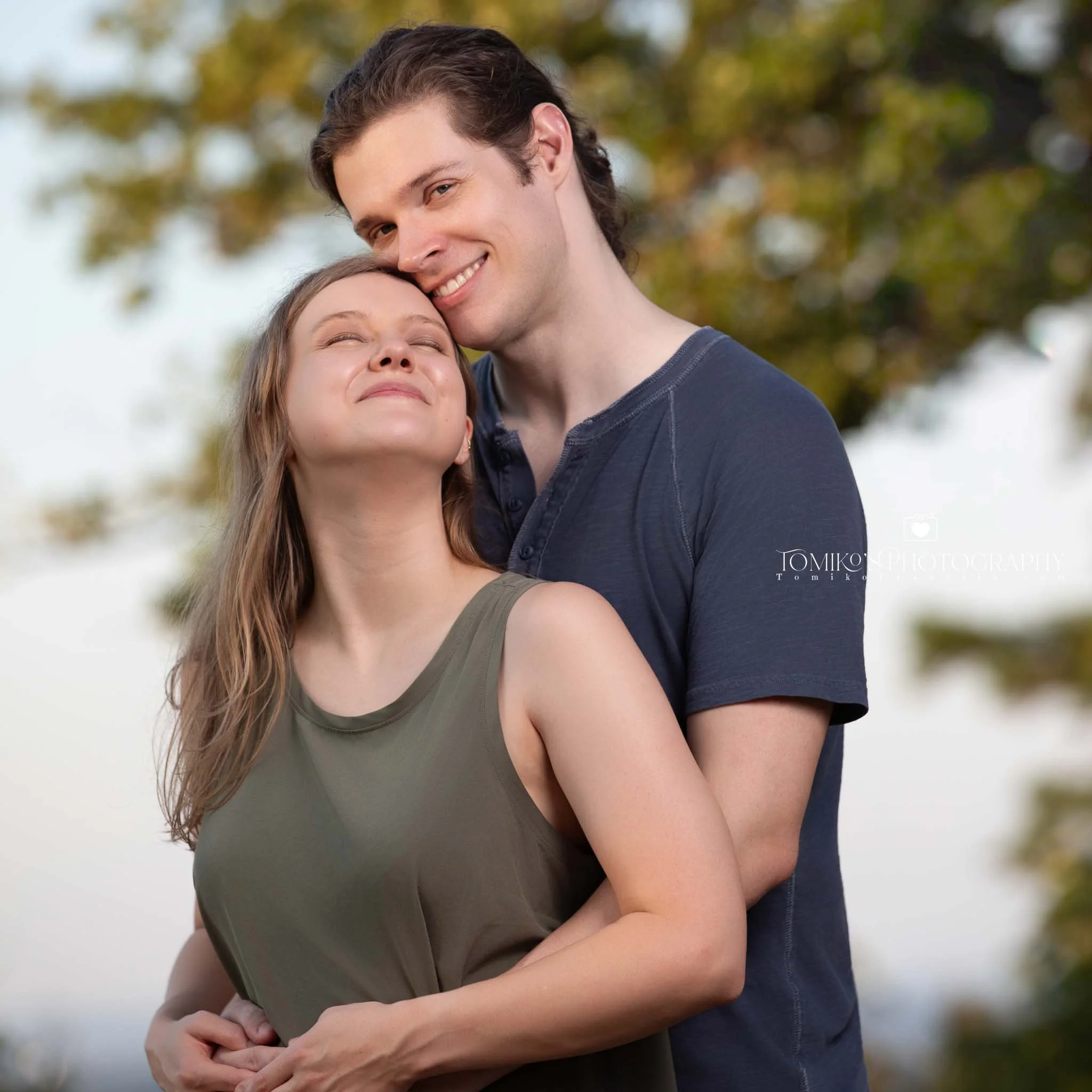 Couple embracing after a surprise proposal at Oak Mountain’s lakeside trail, photographed in warm, natural light.
