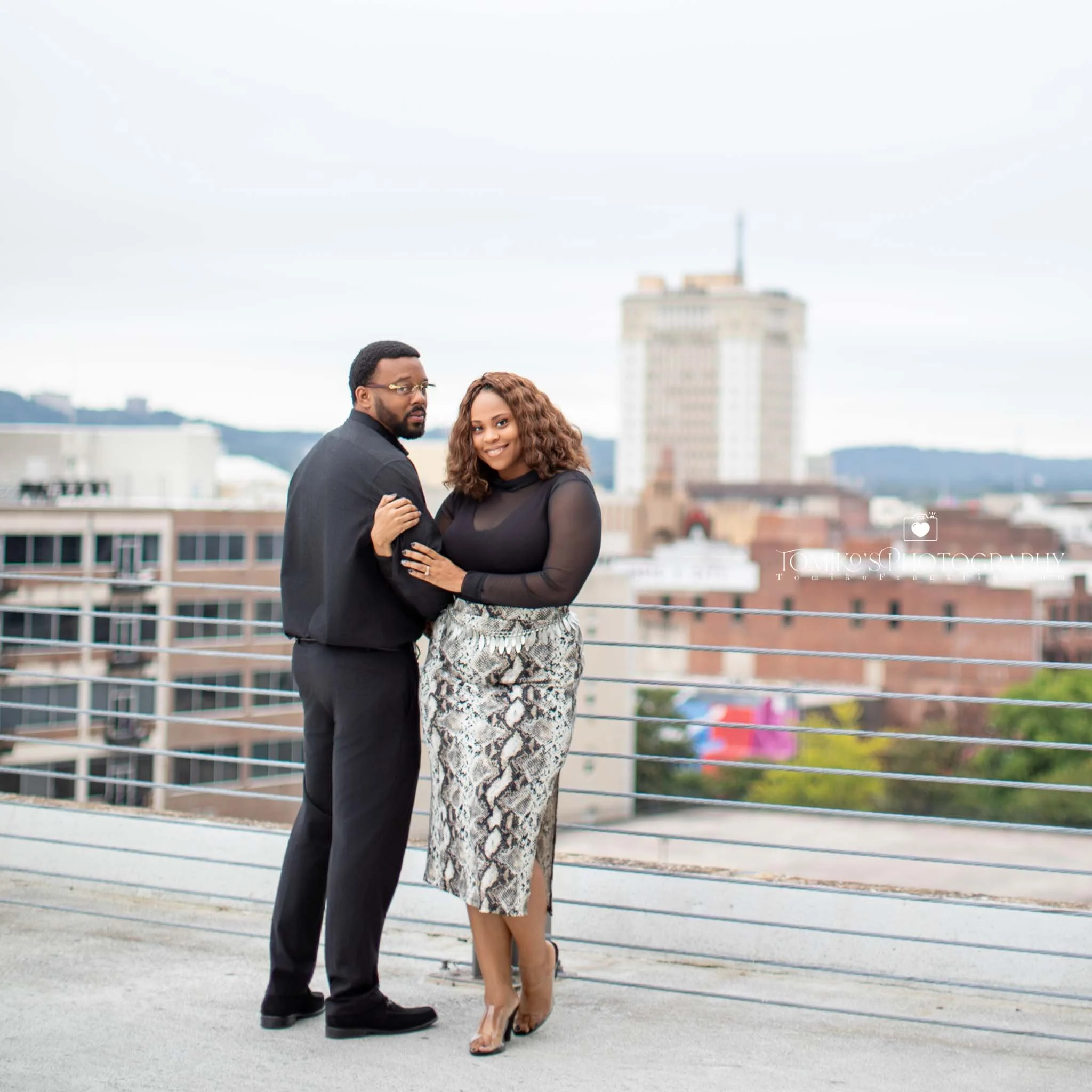 Modern engagement session on a Birmingham rooftop with the skyline glowing behind a smiling couple.