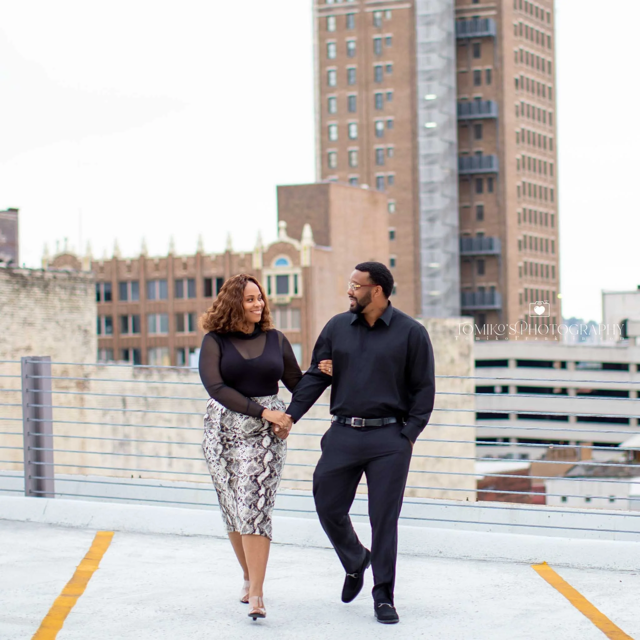 Romantic rooftop engagement photo of a couple sharing a moment with Birmingham’s skyline at golden hour.