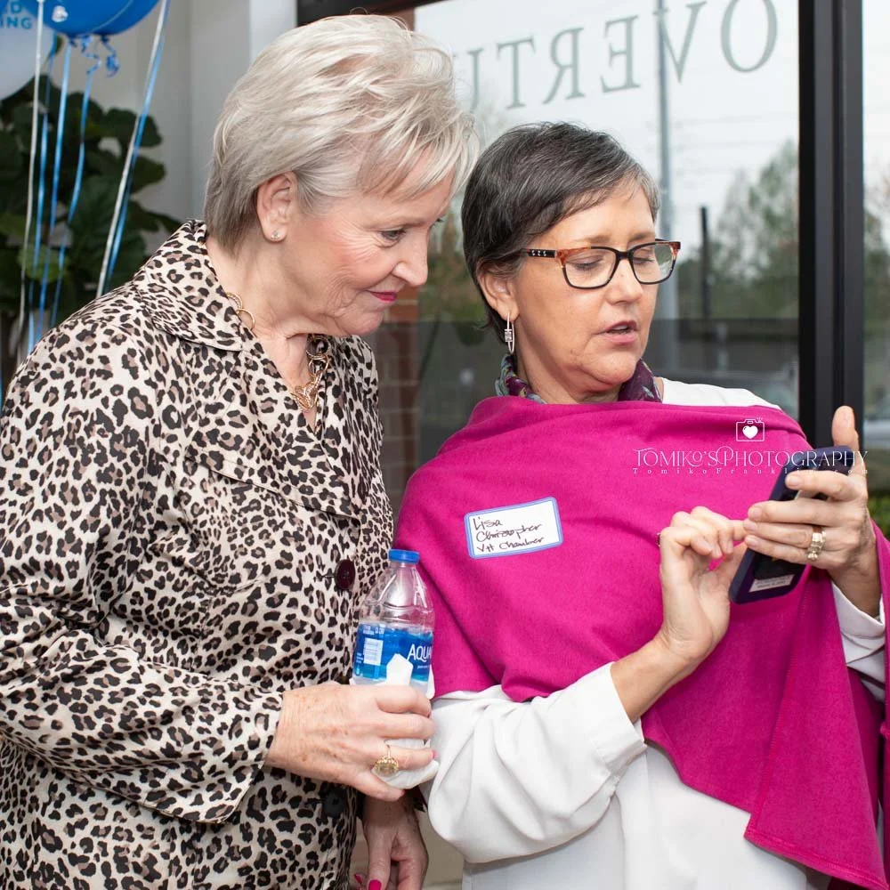 Event photography photo of Two women at a grand opening party in Birmingham, Alabama, looking at an iPhone and capturing the moment.